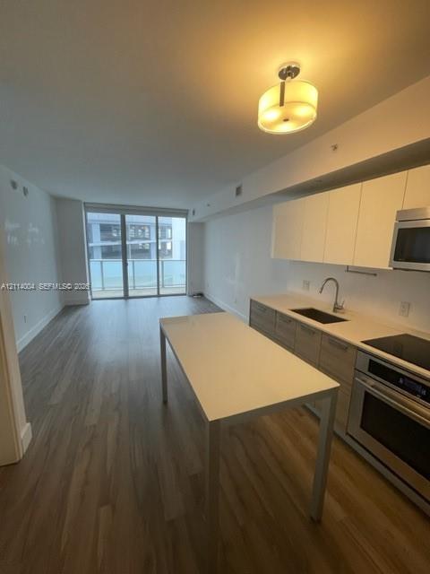 Kitchen featuring flat-panel cabinetry, light-toned countertops, built-in stainless steel appliances, wood-finish flooring, and a sliding glass door to a balcony Kitchen featuring flat-panel cabinetry, light-toned countertops, built-in stainless steel appliances, wood-finish flooring, and a sliding glass door to a balcony