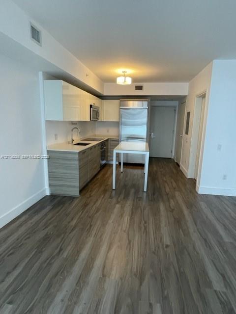 Kitchen featuring high-gloss white upper cabinetry, wood-finish lower cabinetry, stone countertops, stainless steel appliances, and wood-finish flooring Kitchen featuring high-gloss white upper cabinetry, wood-finish lower cabinetry, stone countertops, stainless steel appliances, and wood-finish flooring