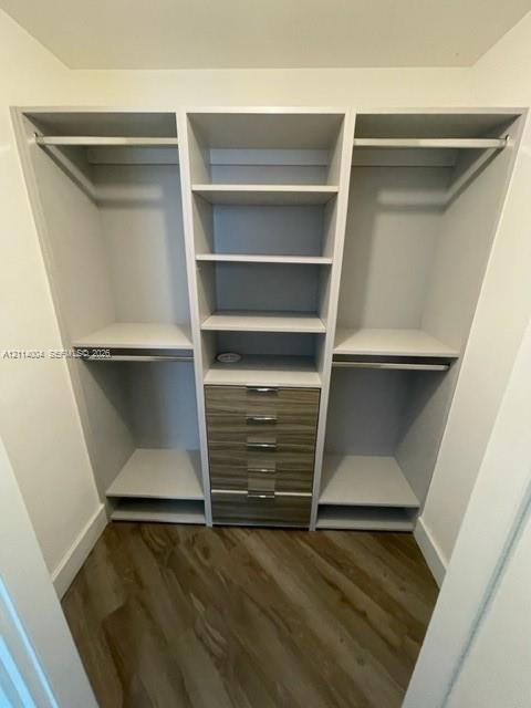 Custom built-in closet organization system featuring white shelving, integrated hanging rods, a five-drawer wood-finish cabinet unit with metallic pulls, and wood-finish flooring