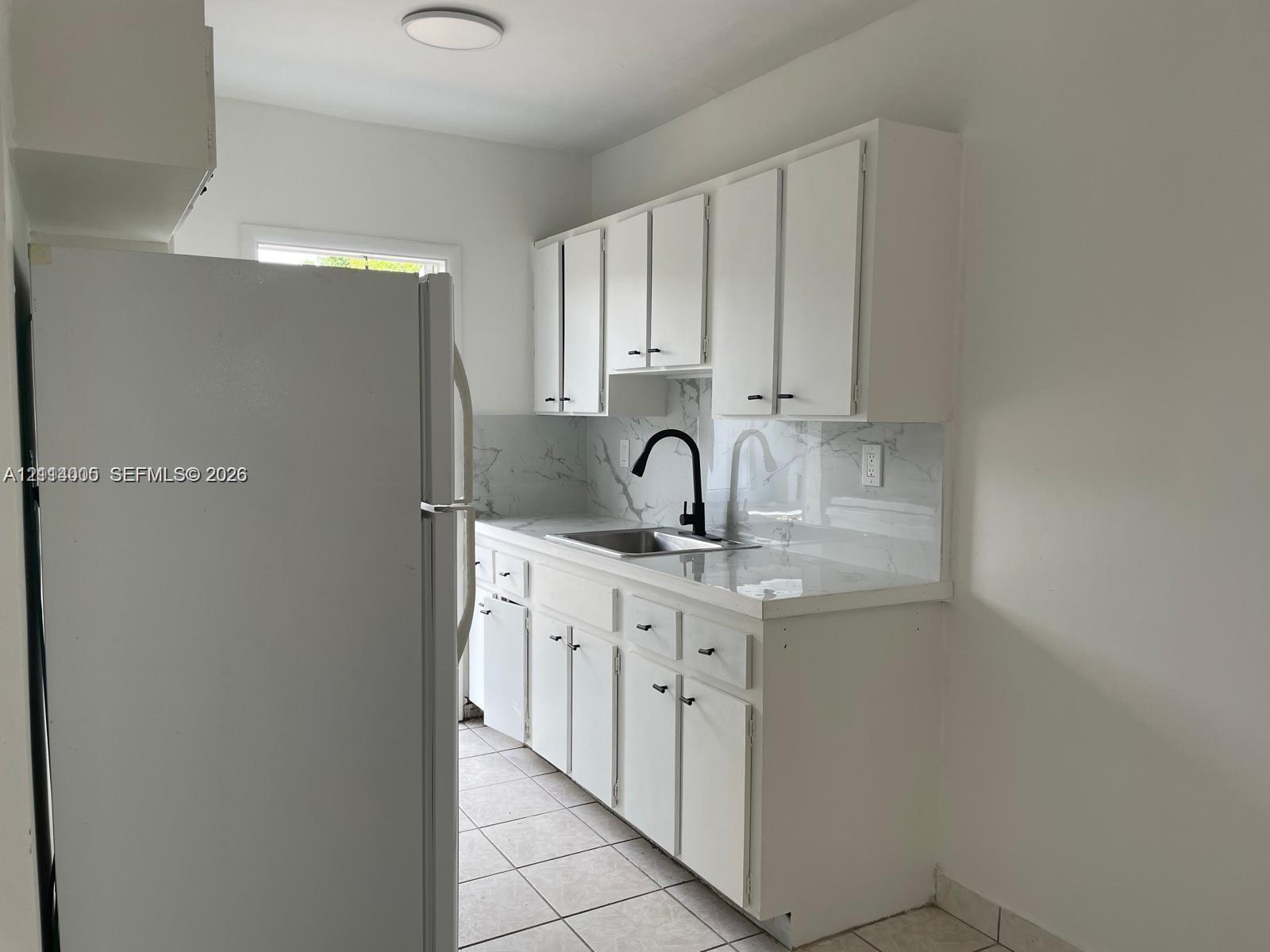 Kitchen featuring white cabinetry, stone-surface countertops, full-height stone backsplash, matte black faucet, and ceramic tile flooring