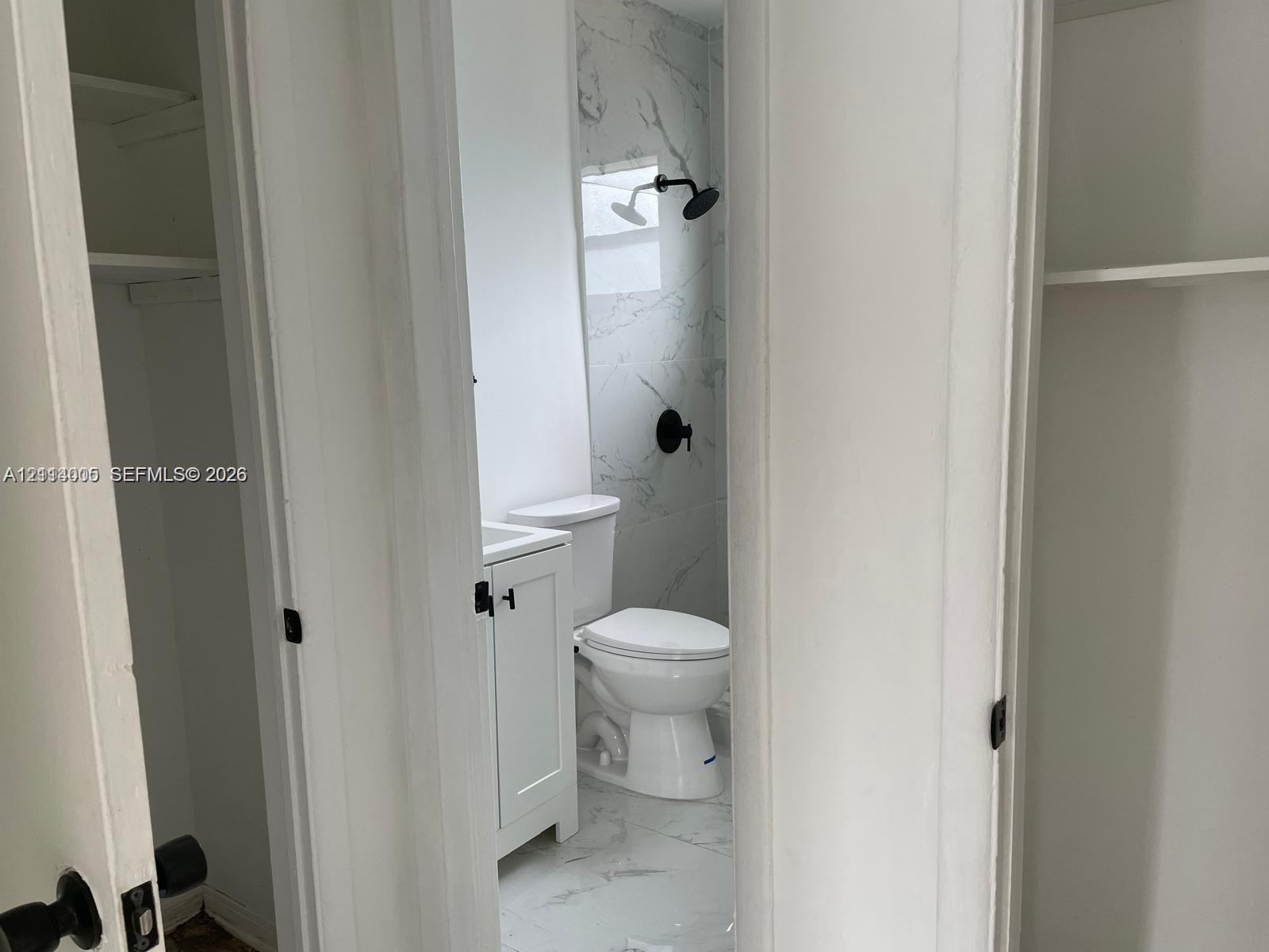 Bathroom featuring a vanity with white cabinetry, light-toned stone-patterned tile flooring, full-height wall-surround tile, and matte black plumbing fixtures