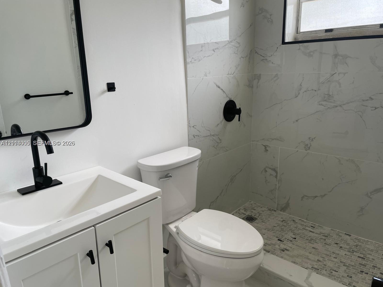Bathroom featuring a white vanity cabinet, rectangular vessel sink with a matte black faucet, framed vanity mirror, walk-in shower with large-format wall tiling, and mosaic-tiled shower flooring