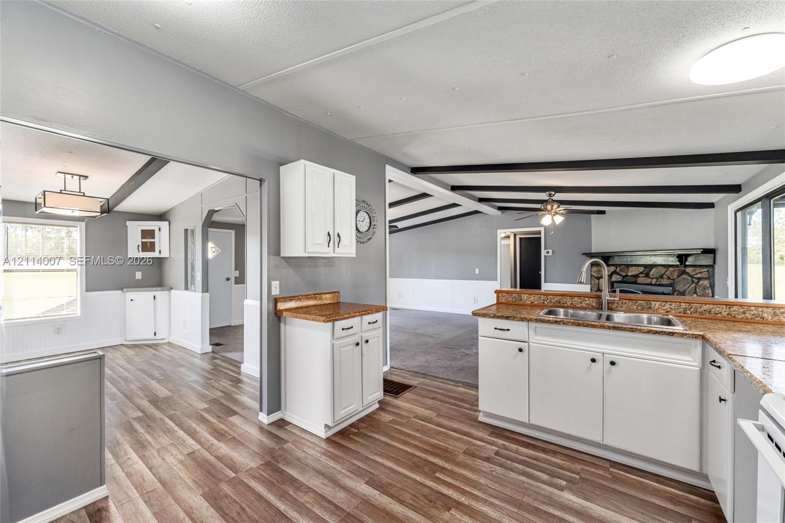 Kitchen featuring white cabinetry, stone-finish countertops, dual-basin stainless steel sink, wood-finish flooring, and decorative ceiling beams