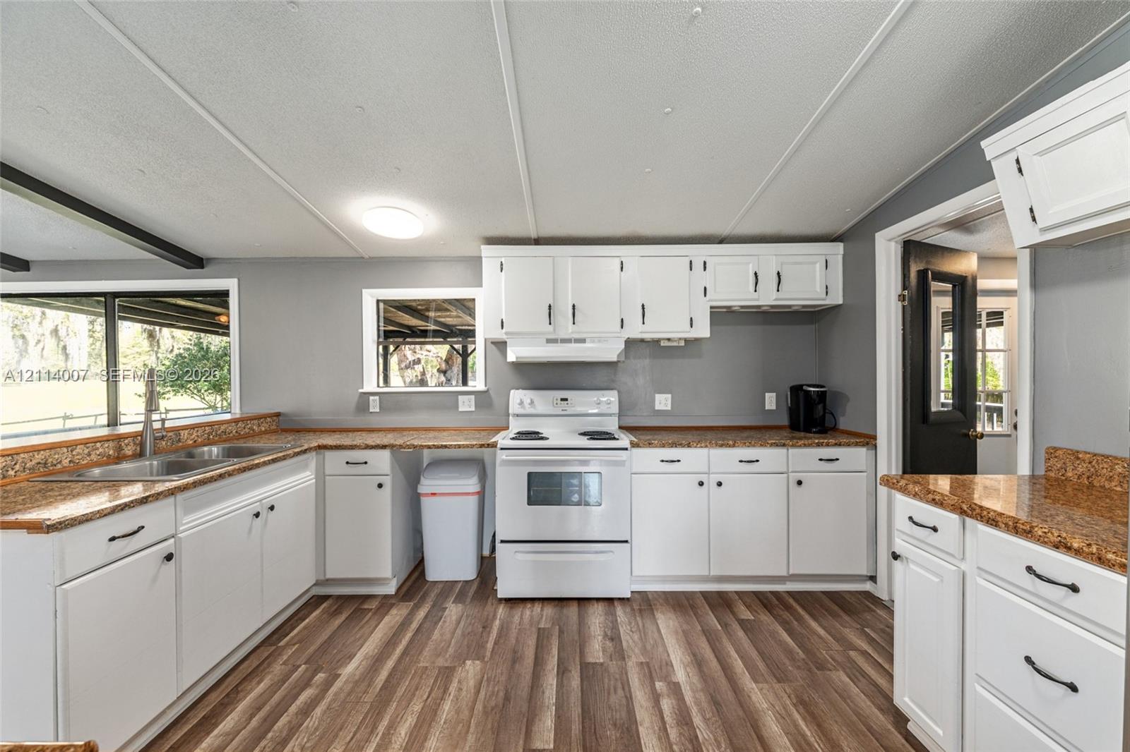 Kitchen featuring white shaker-style cabinetry, speckled solid-surface countertops, wood-finish flooring, a white freestanding range, and stainless steel dual-basin sink