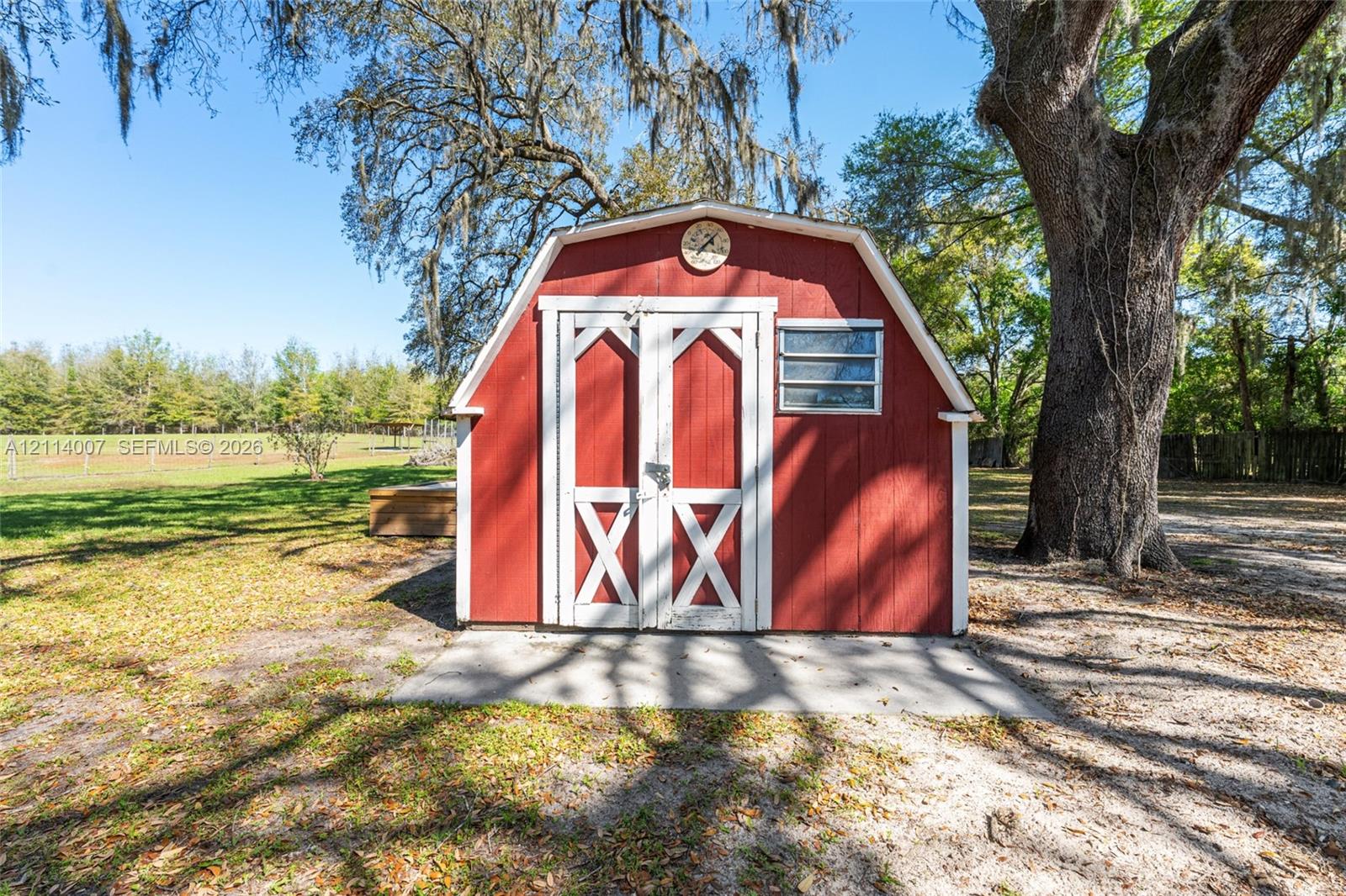 Gambrel-style outbuilding featuring red wood-finish siding, white trim, double entry doors, and a horizontal louvered window set on a concrete foundation