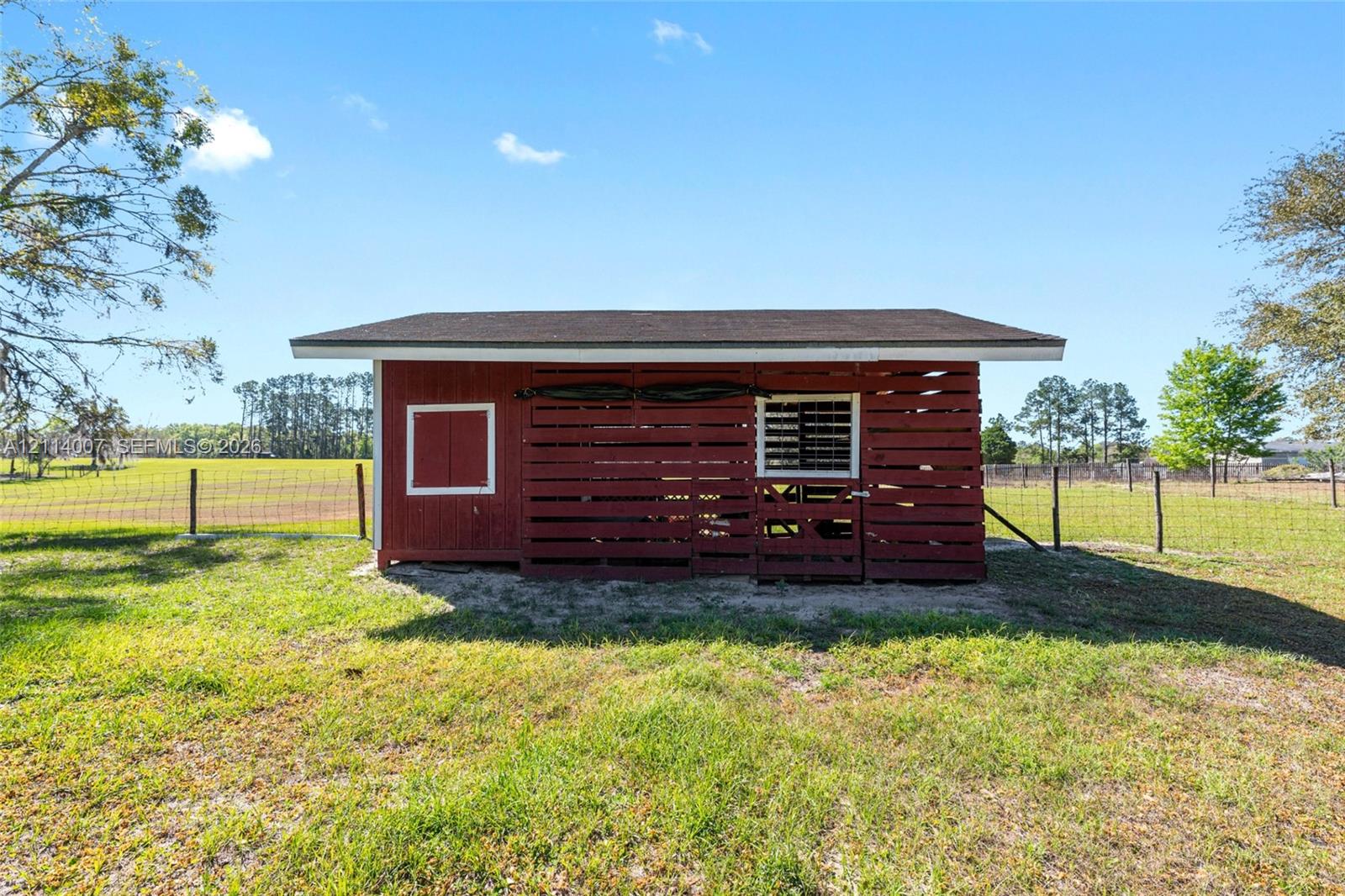 Red wooden outbuilding featuring horizontal slat siding, a pitched roof, and wire-fenced perimeter grounds