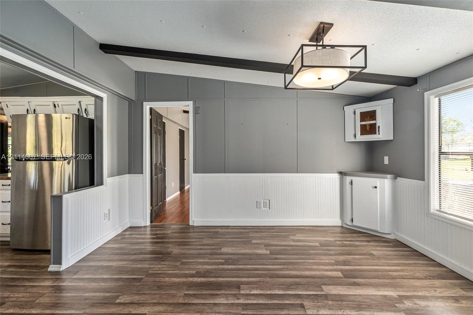 Interior space featuring wood-finish flooring, beadboard wainscoting, exposed ceiling beam, geometric metal-frame light fixture, and built-in corner cabinetry