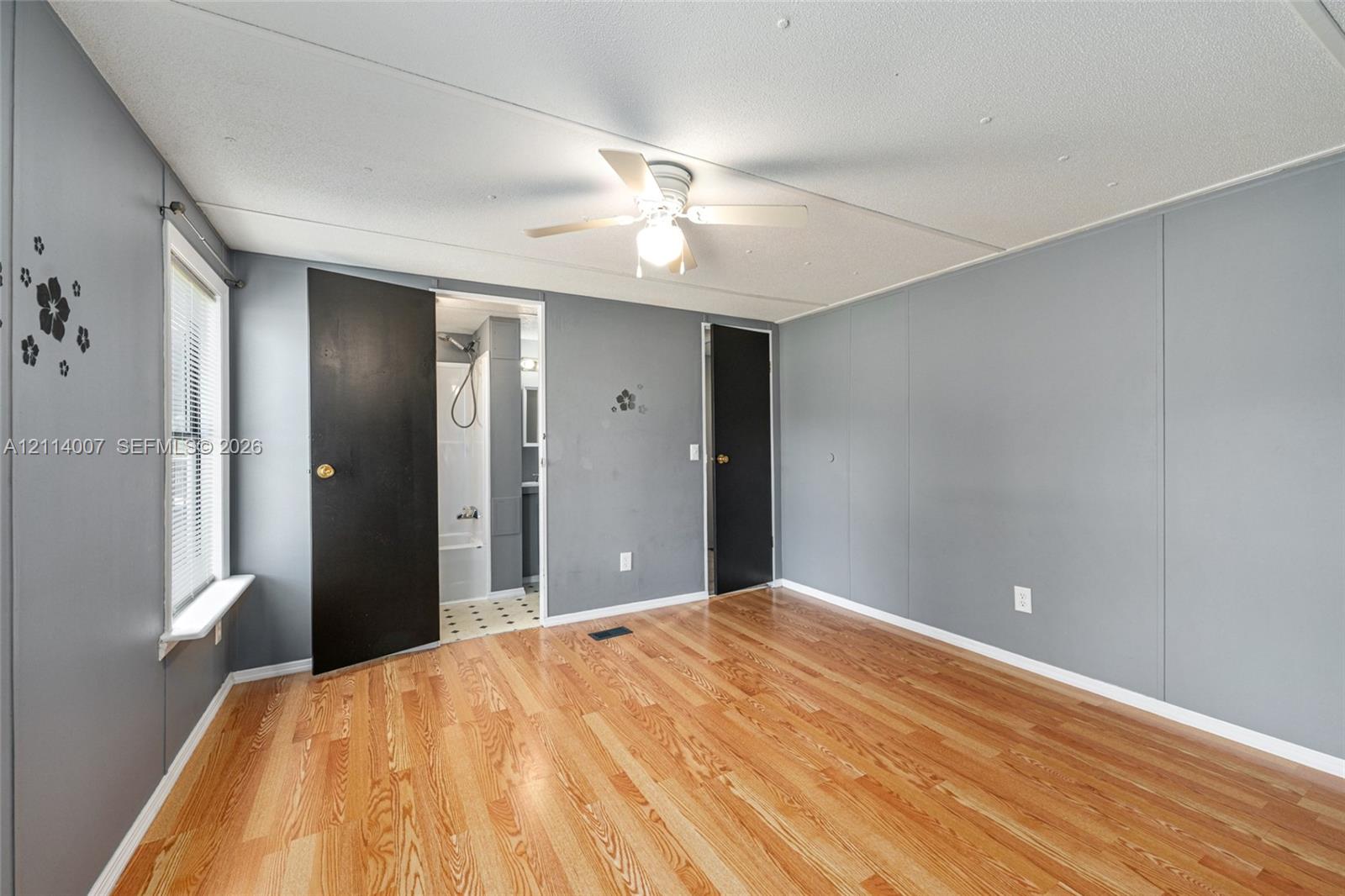 Room featuring wood-finish flooring, a ceiling fan with integrated lighting, window with sill, and two solid-core doors