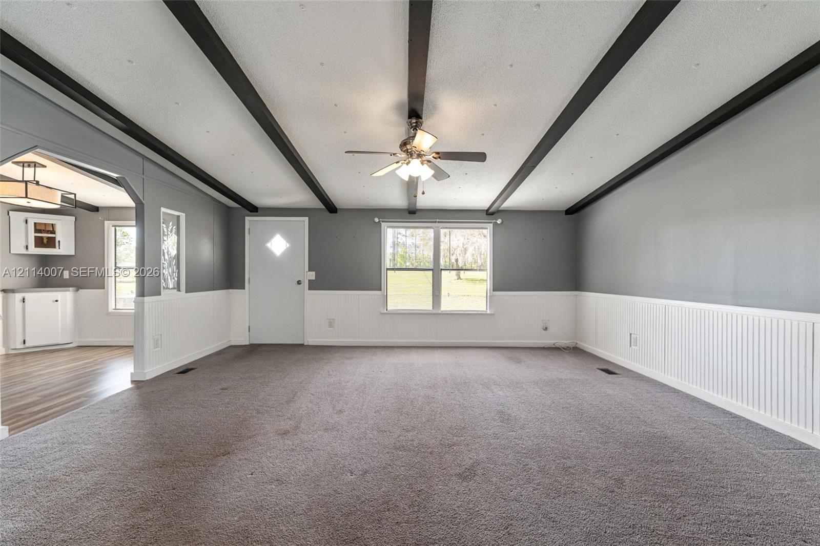 Room featuring high-contrast decorative ceiling beams, beadboard wainscoting, and a central ceiling fan