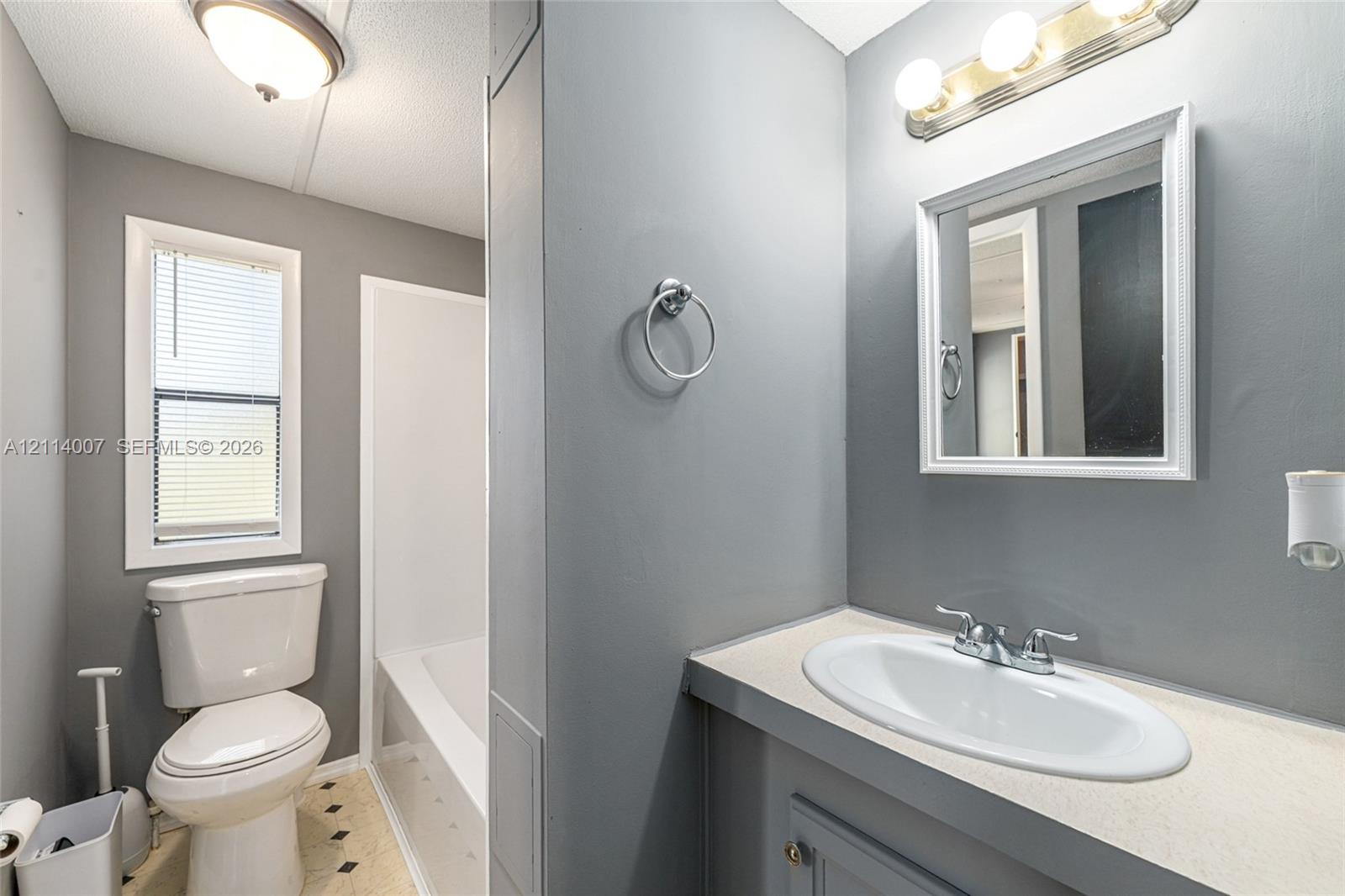 Bathroom featuring a vanity with a white integrated oval sink, a wall-mounted three-light fixture, a framed mirror, a separate tub-shower combination, and a window