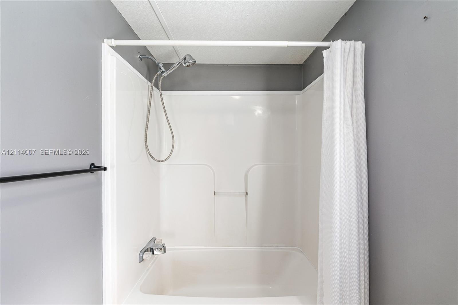 Bathtub with an integrated white surround, wall-mounted hand-held shower fixture, and a built-in recessed shelf
