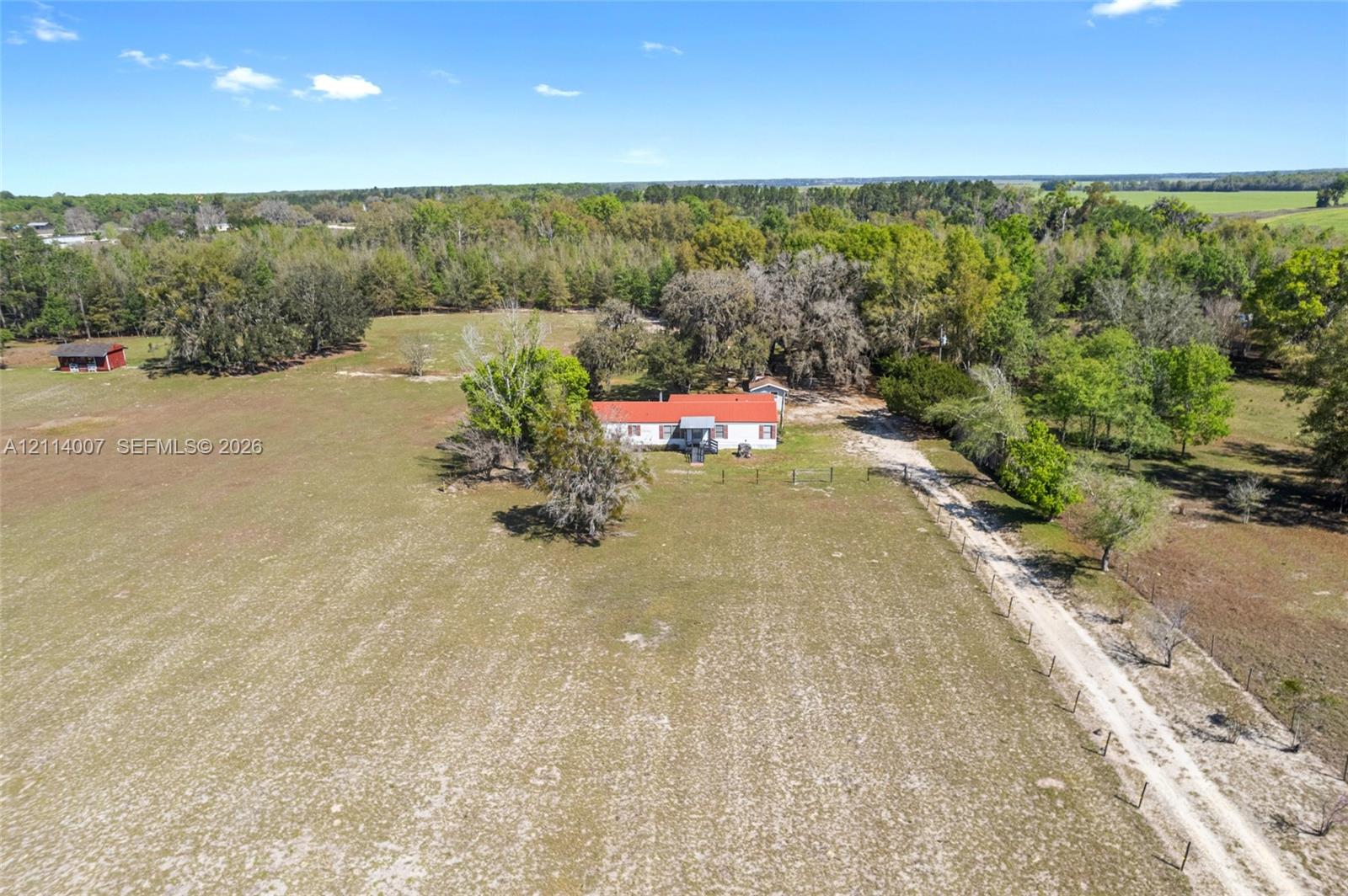 Single-story residence featuring a metal roof, expansive acreage, mature trees, and a private gravel drive