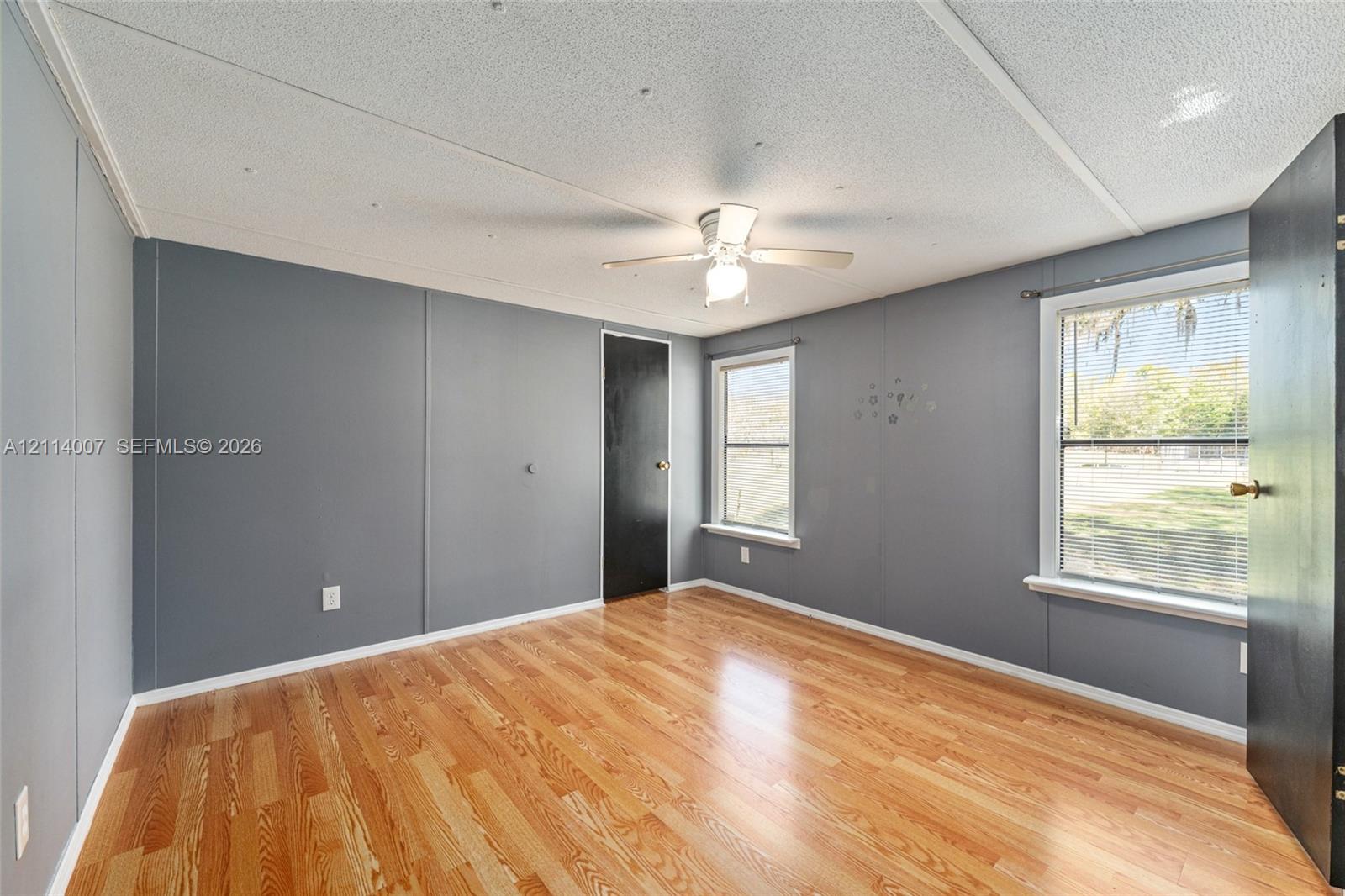 Room featuring wood-finish flooring, dual windows, matte black interior doors, and a ceiling fan with light fixture