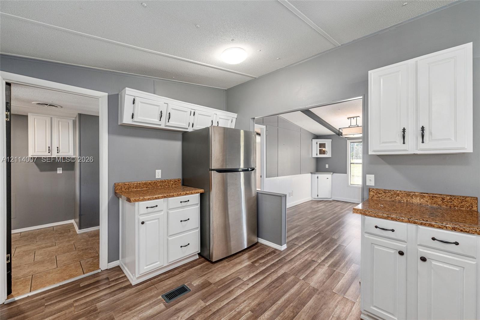 Kitchen featuring white cabinetry, speckled stone-finish countertops, stainless steel refrigerator, and wood-finish flooring