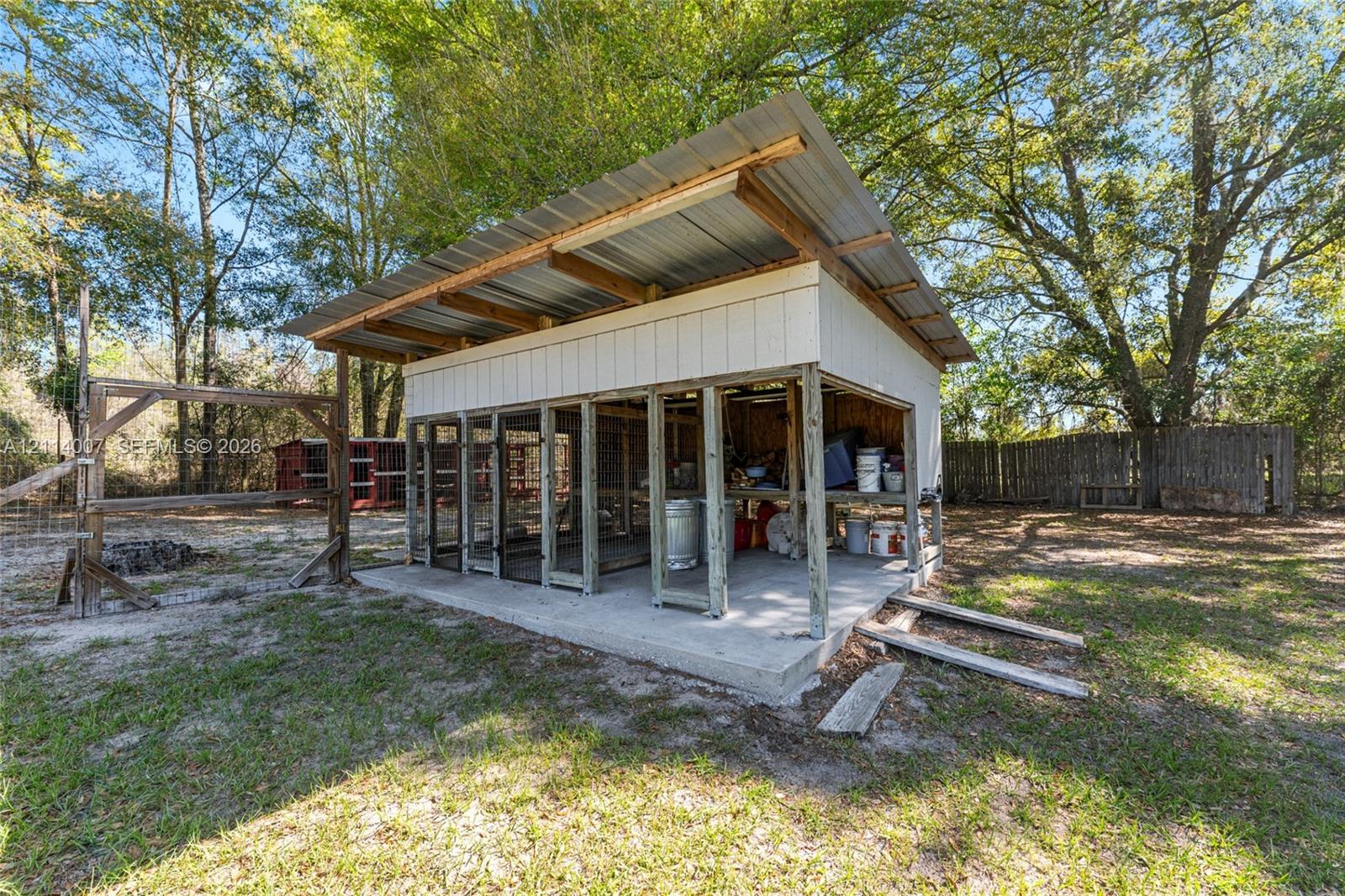 Outdoor structure featuring a concrete foundation, shed-style metal roofing, vertical siding, and an open-frame design with wire mesh panels