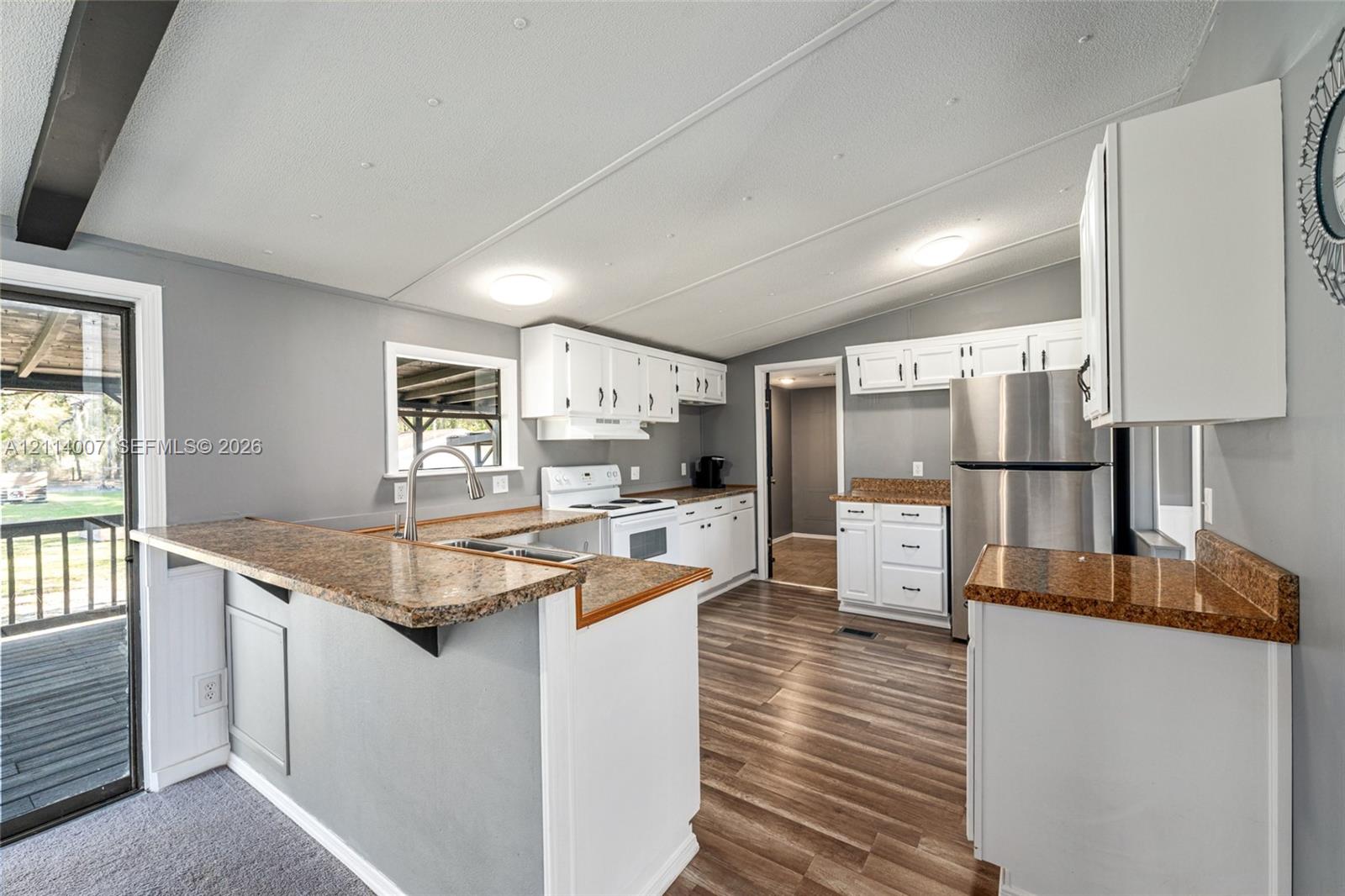 Kitchen featuring white shaker-style cabinetry, stone-finish countertops, stainless steel appliances, and wood-finish flooring