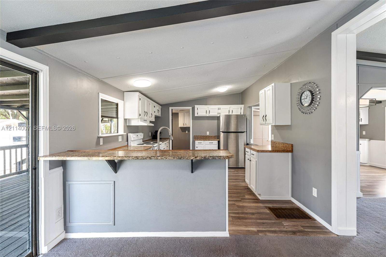 Kitchen featuring white cabinetry, stone-finish countertops, stainless steel appliances, a breakfast bar, and wood-finish flooring