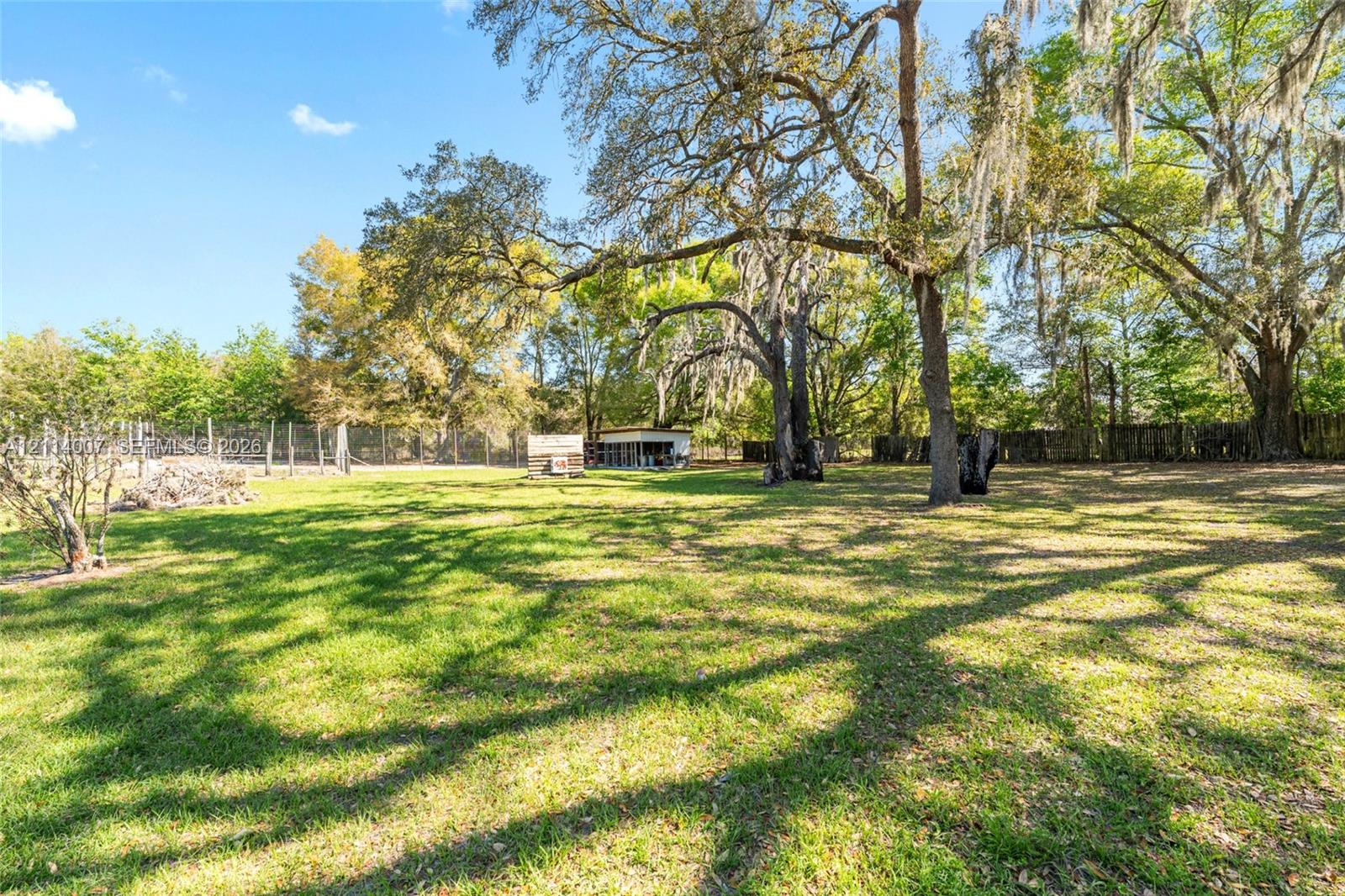 Expansive level grounds featuring mature shade trees, perimeter fencing, and a detached outbuilding