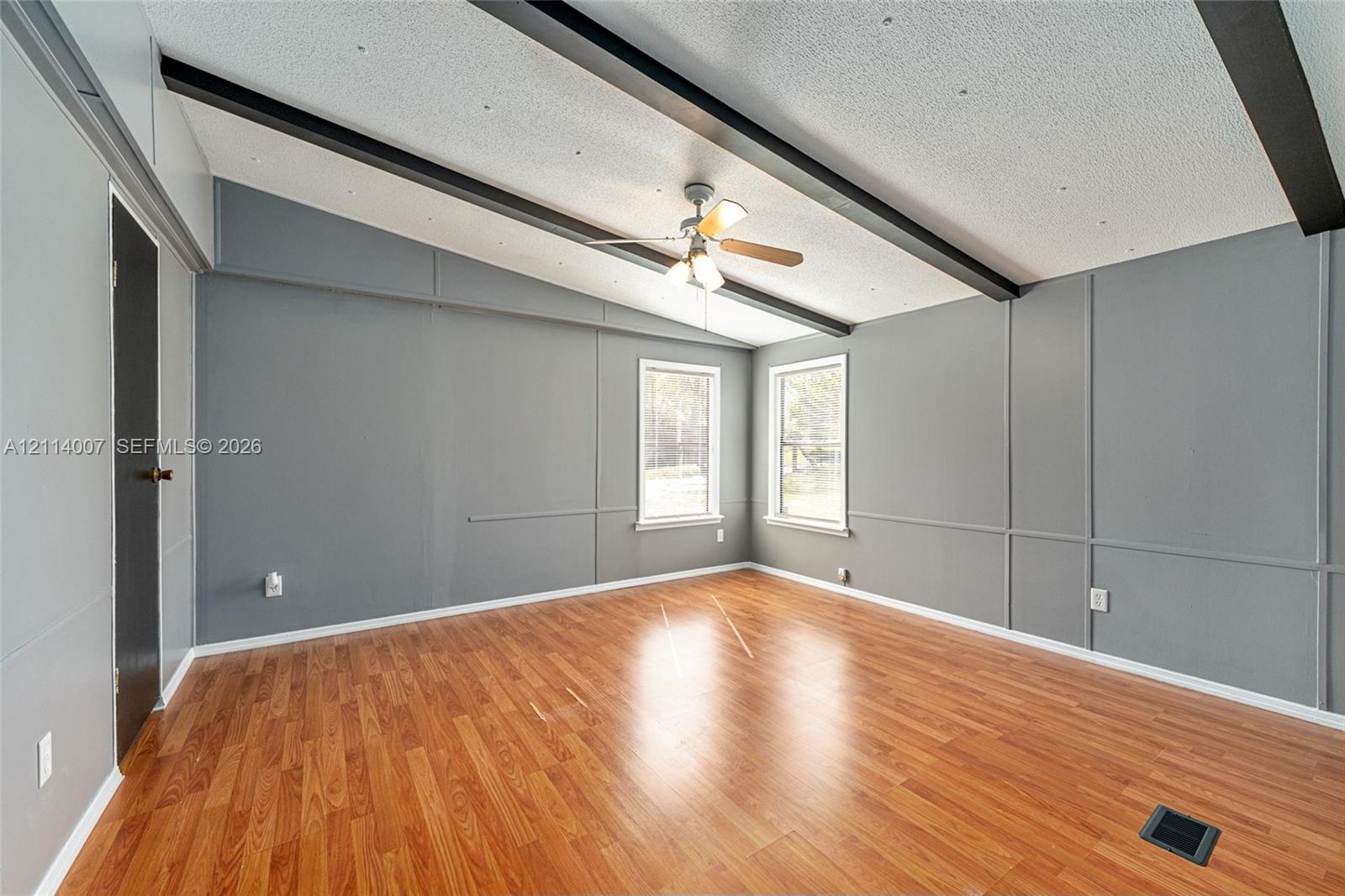 Vaulted ceiling featuring exposed dark beams, wood-finish flooring, wainscoting-style wall paneling, and a central ceiling fan with integrated lighting