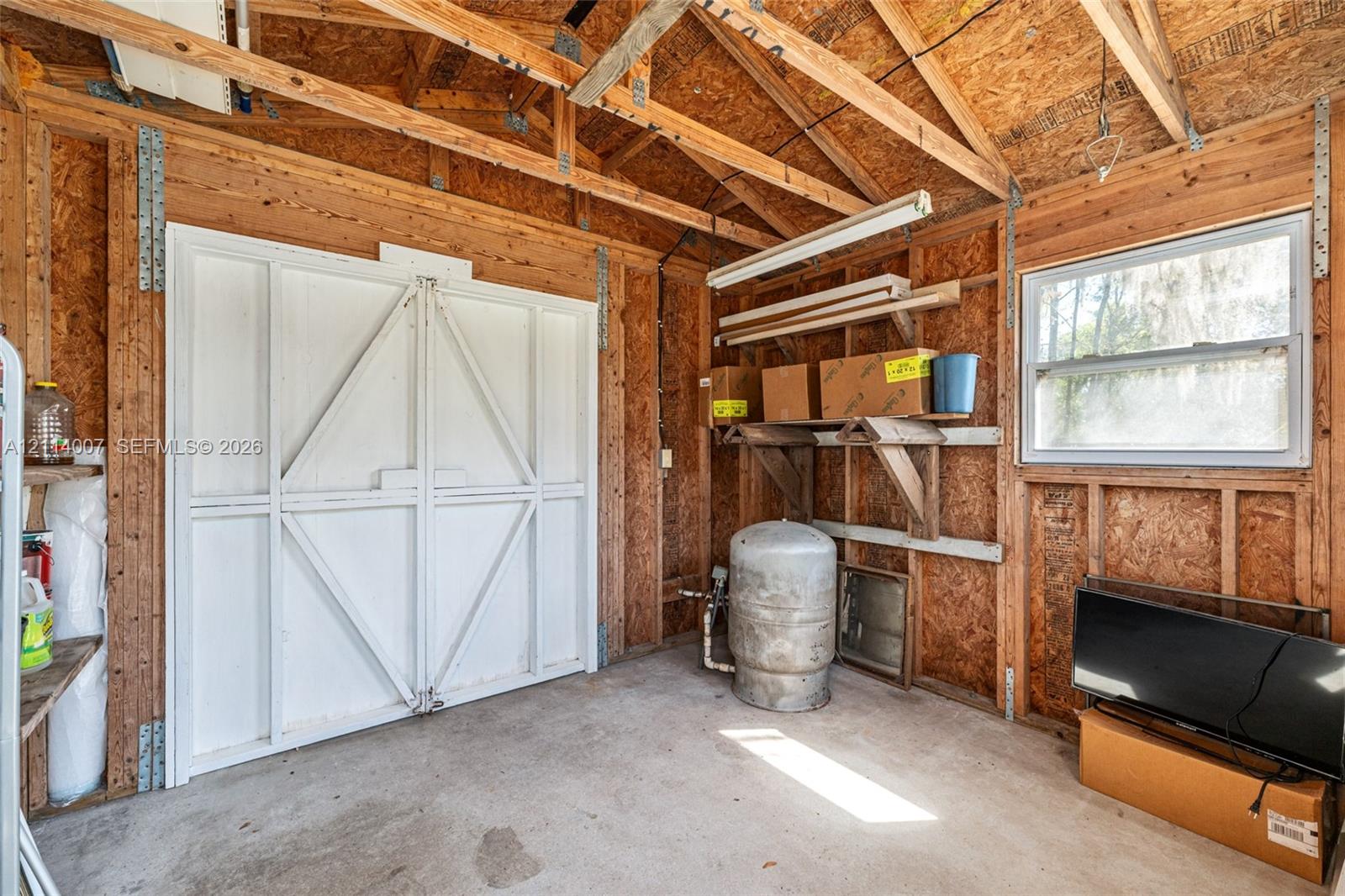 Utility shed featuring exposed wood-stud construction, concrete flooring, double-door entry, and a single-pane window