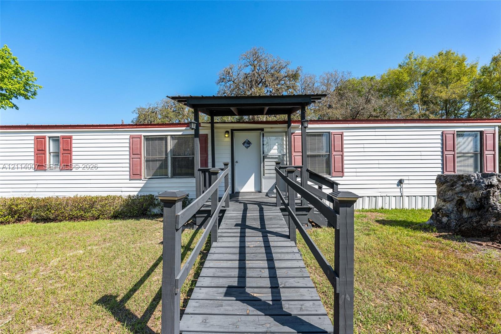 Exterior featuring white horizontal siding, dark-toned shutters, a covered front entryway, and a wooden accessibility ramp with handrails