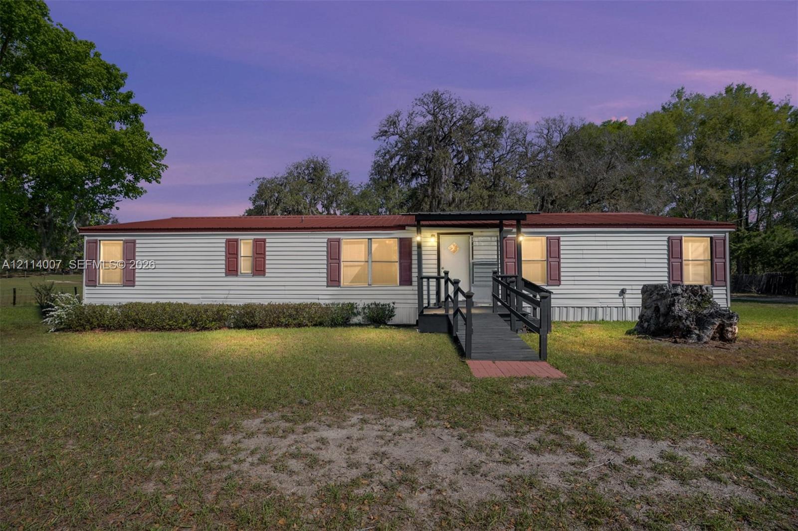 Single-story exterior featuring light-colored horizontal siding, dark-toned shutters, a metal roof, and an elevated entry landing with a staircase and railing