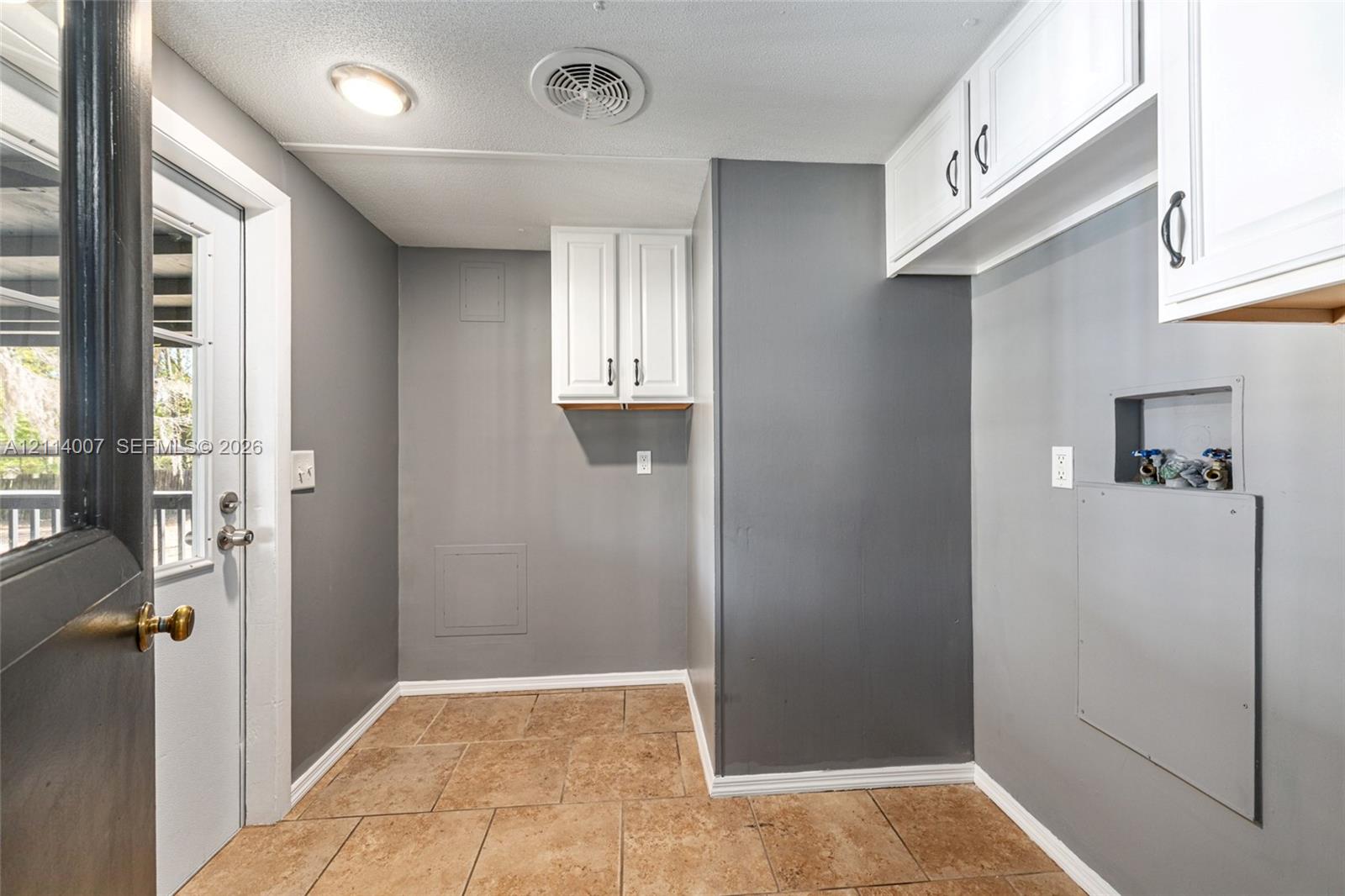 Utility room featuring tile flooring, white upper cabinetry, dedicated plumbing hookups, and a glass-paneled exterior door