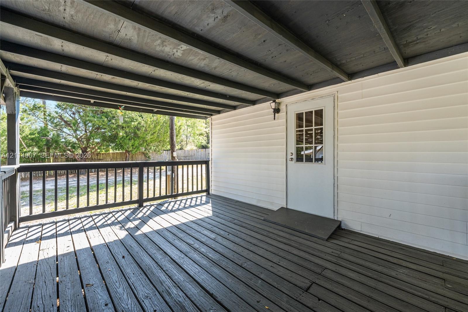 Covered porch featuring dark wood-finish decking, horizontal vinyl siding, a multi-pane glass door, and a perimeter railing