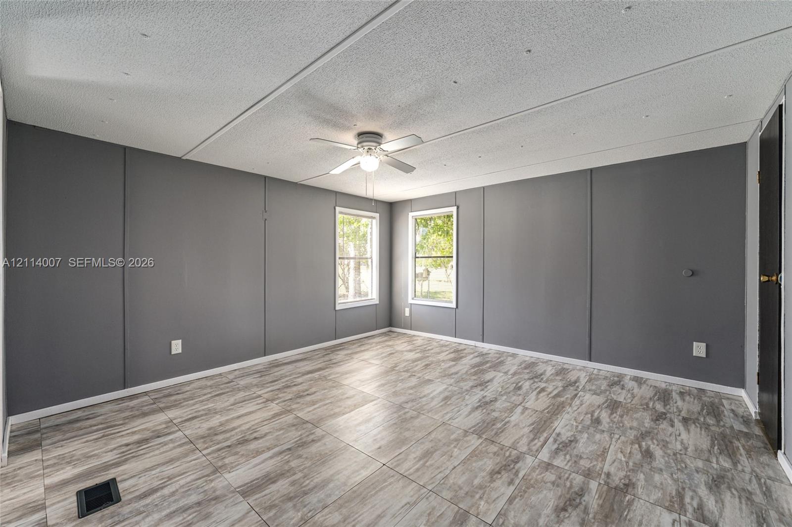 Room featuring wood-finish tile flooring, painted gray panel walls, two double-hung windows, and a central ceiling fan
