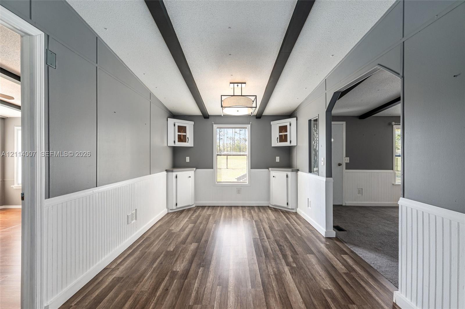 Interior space featuring wood-finish flooring, beadboard wainscoting, built-in corner cabinetry, exposed ceiling beams, and a drum-style pendant light fixture