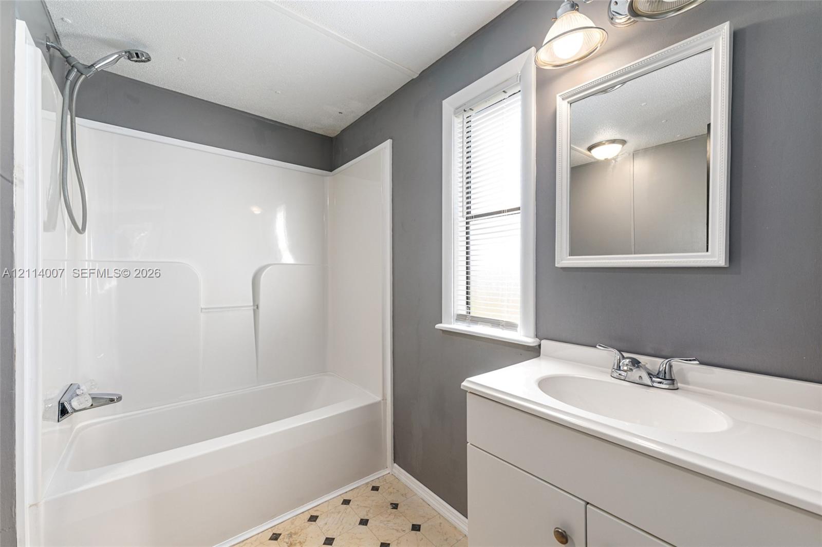 Bathroom featuring a white tub-shower combination, a vanity with a white integrated sink, a wall-mounted mirror, and patterned tile flooring