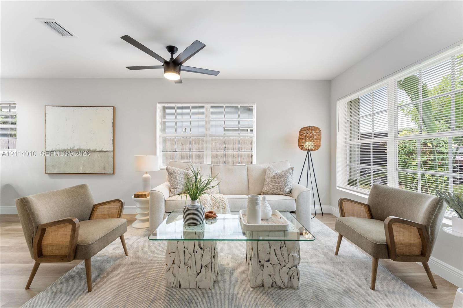 Light-filled interior featuring expansive multi-pane windows, wood-finish flooring, and a central matte black ceiling fan with integrated lighting