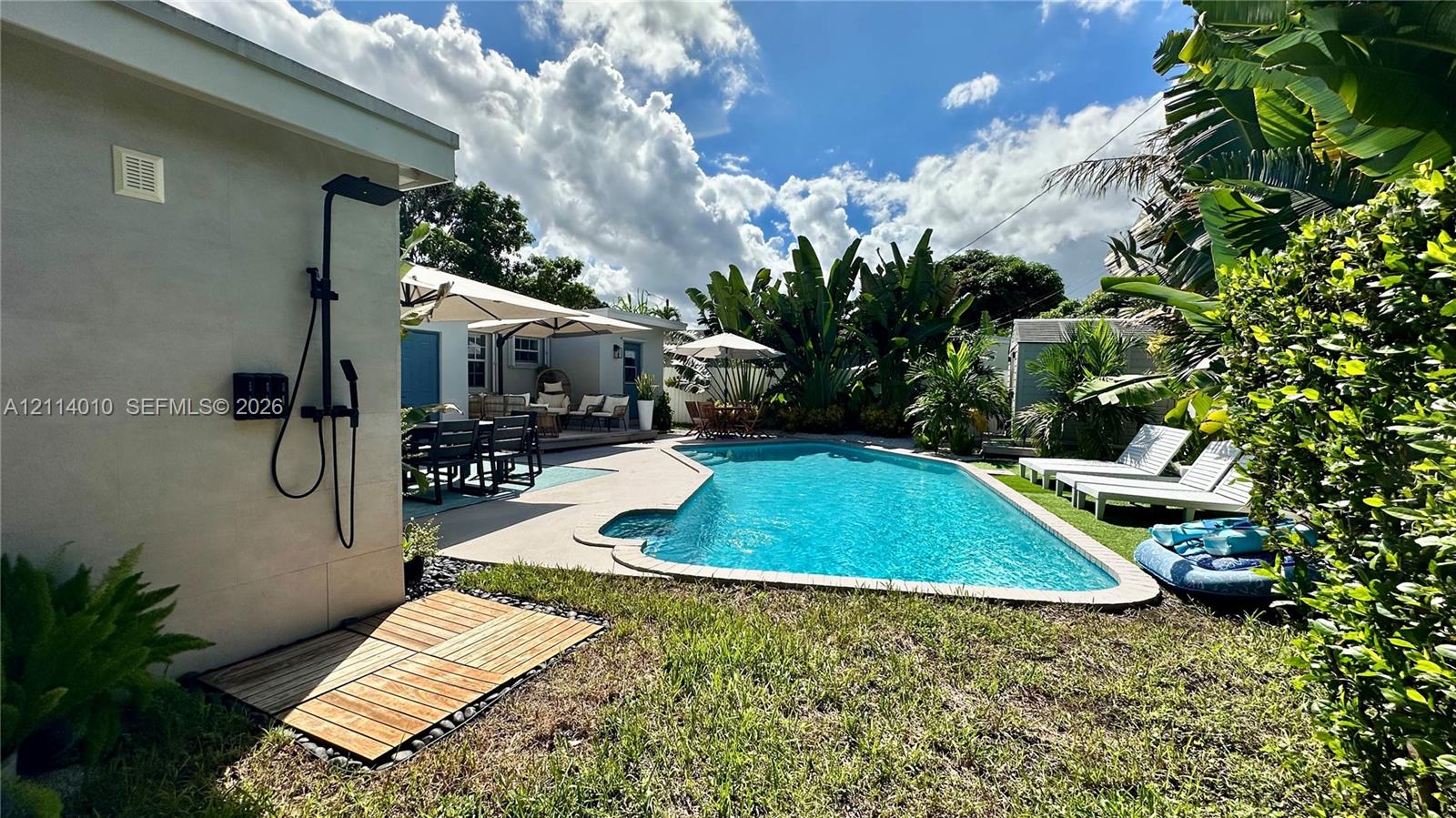 Outdoor space featuring a swimming pool, wood-slat shower base, wall-mounted matte black exterior shower fixture, and landscaped perimeter foliage