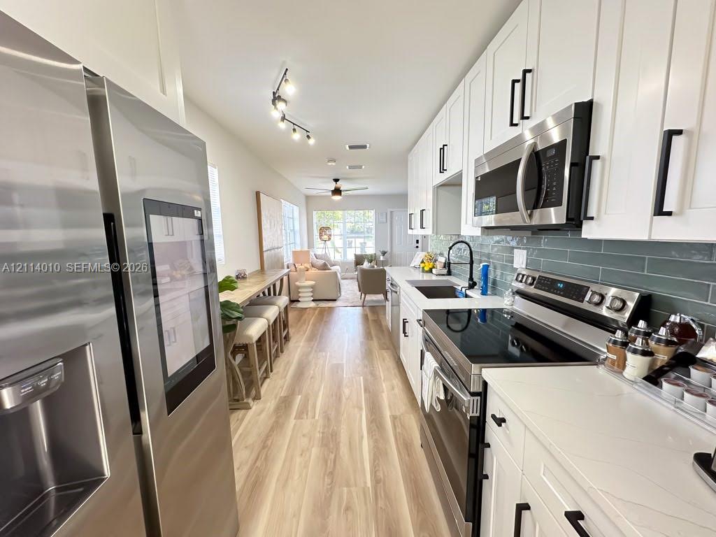 Kitchen featuring white shaker-style cabinetry, quartz countertops, stainless steel appliances, a green subway tile backsplash, and wood-finish flooring