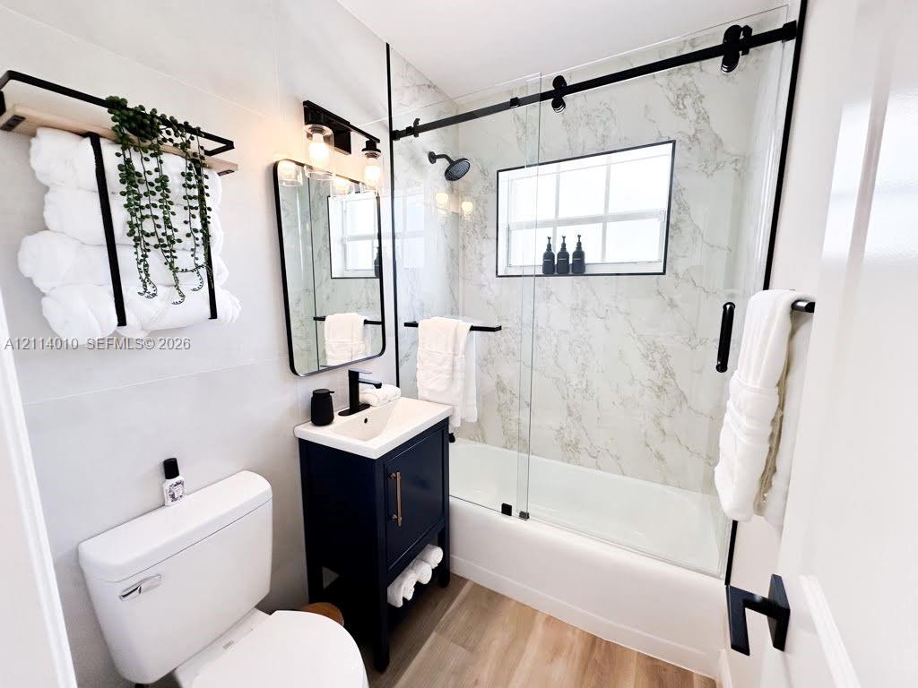 Bathroom featuring a vanity with a rectangular sink, stone-patterned shower surround, glass sliding shower door with matte black hardware, and wood-finish flooring