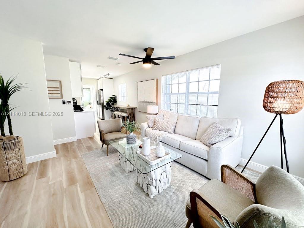 Living area featuring wood-finish flooring, a matte black multi-blade ceiling fan, and large grid-pane windows