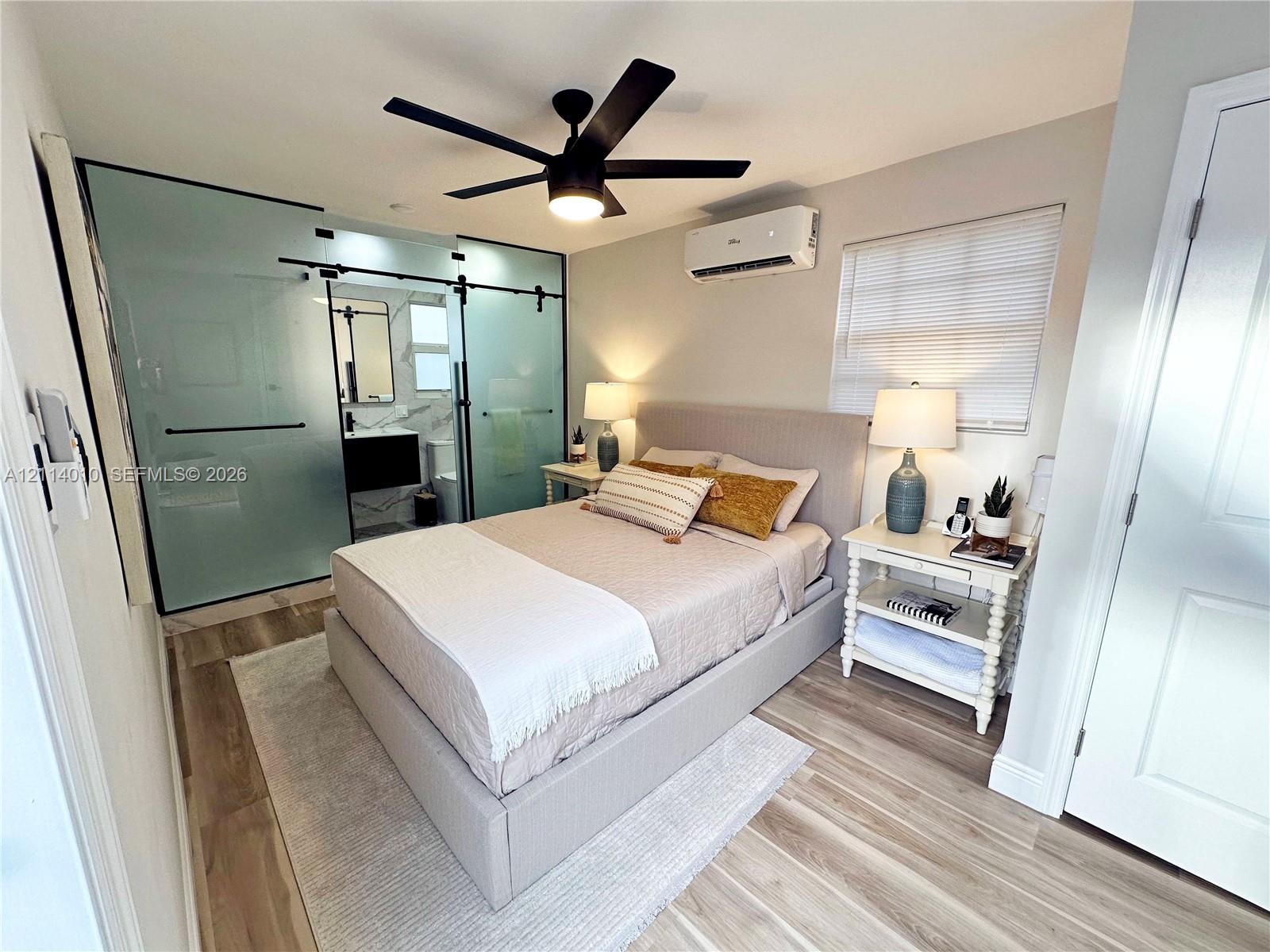 Frosted glass sliding barn doors, wood-finish flooring, ceiling fan with integrated lighting, and wall-mounted ductless air conditioning unit