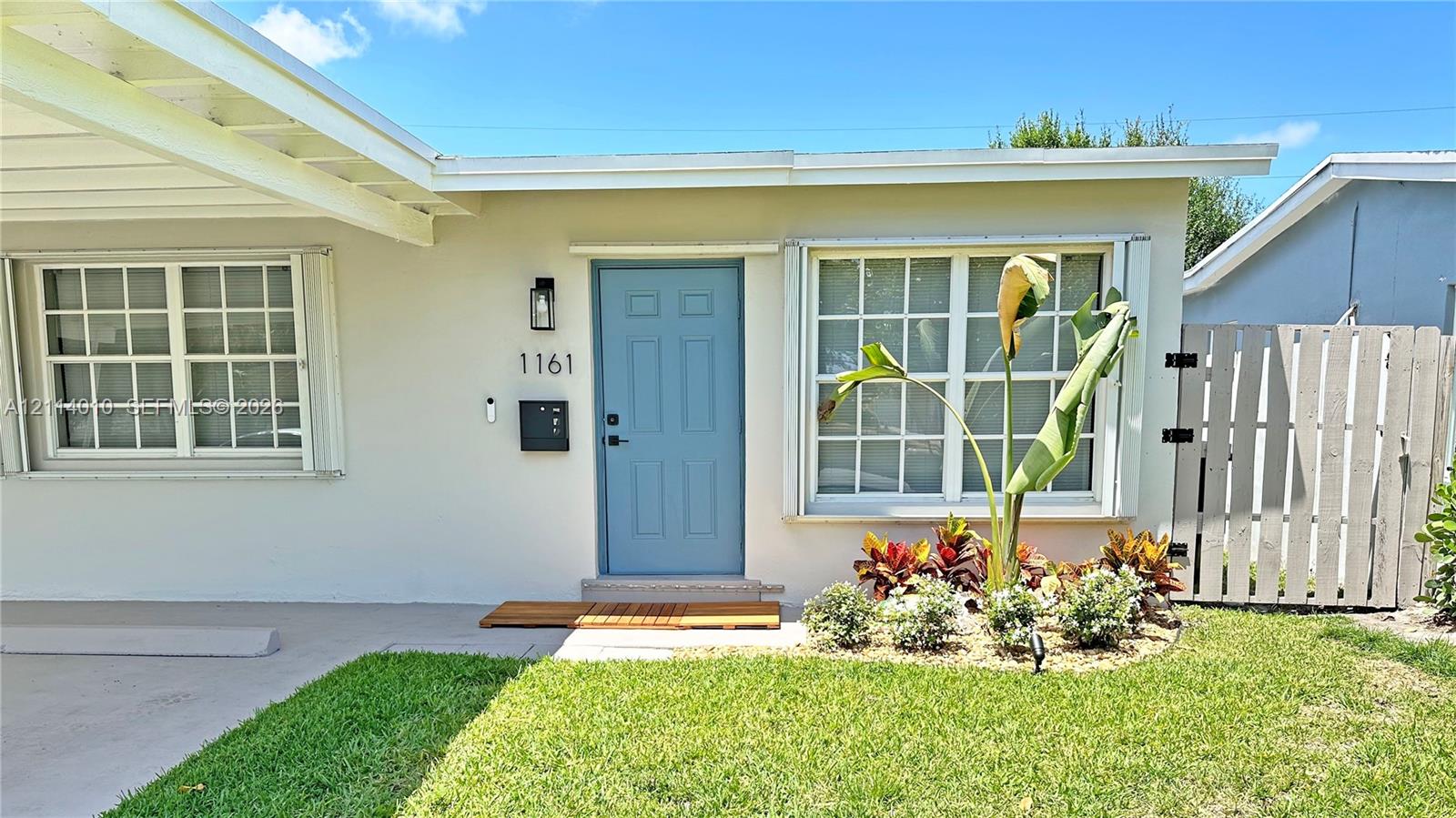 Exterior facade featuring a covered carport, multi-pane windows, a paneled front entry door, and a privacy fence