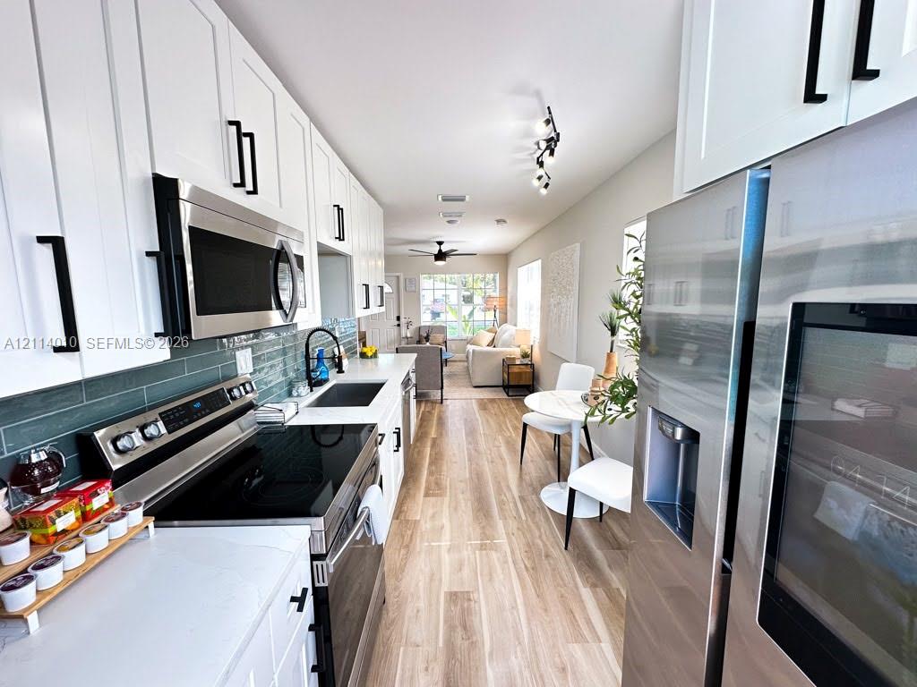 Kitchen featuring white Shaker-style cabinetry, stainless steel appliances, wood-finish flooring, quartz countertops, and a blue subway tile backsplash