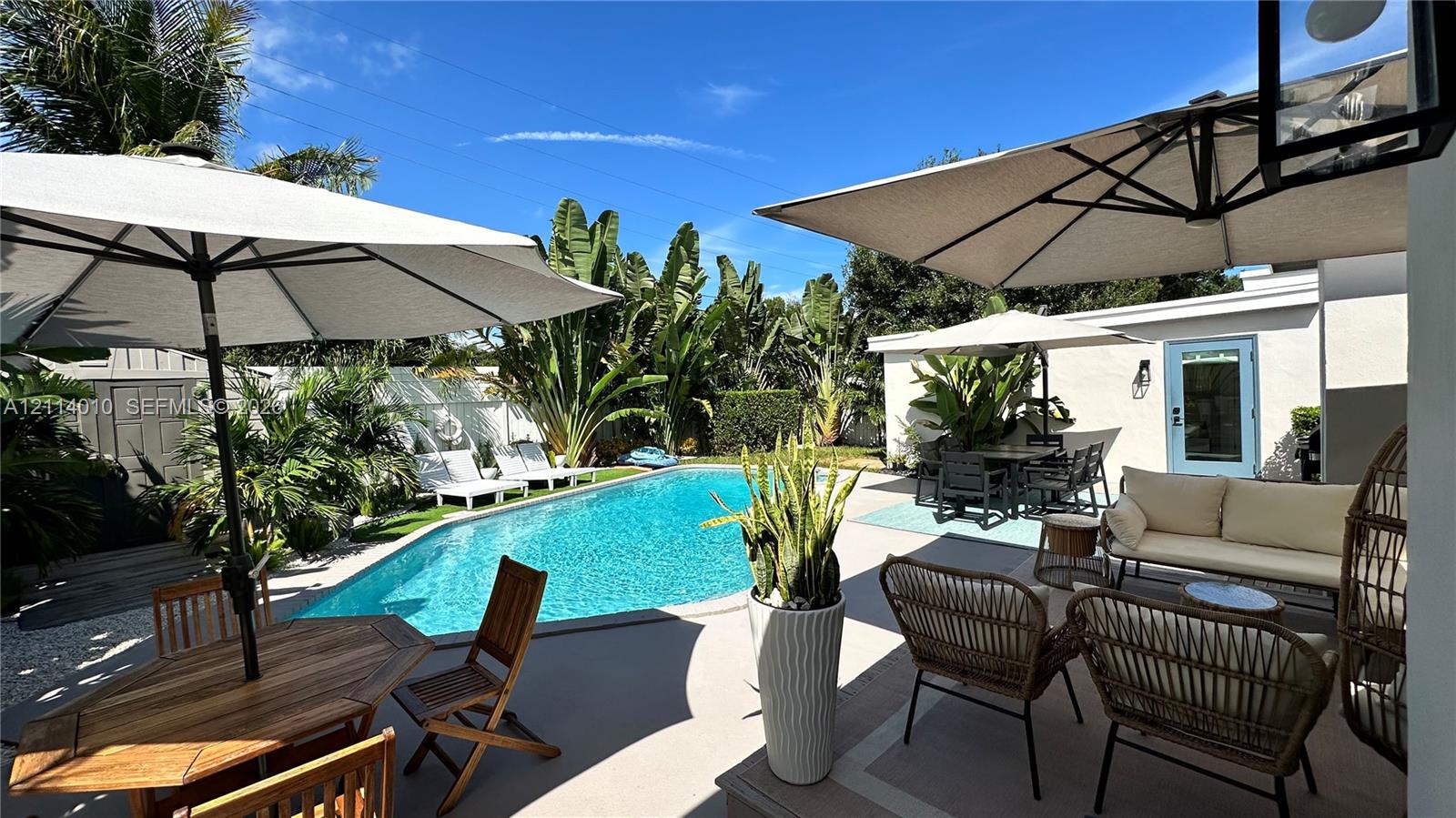 Outdoor space featuring a swimming pool, concrete patio, white vinyl perimeter fencing, and mature tropical landscaping