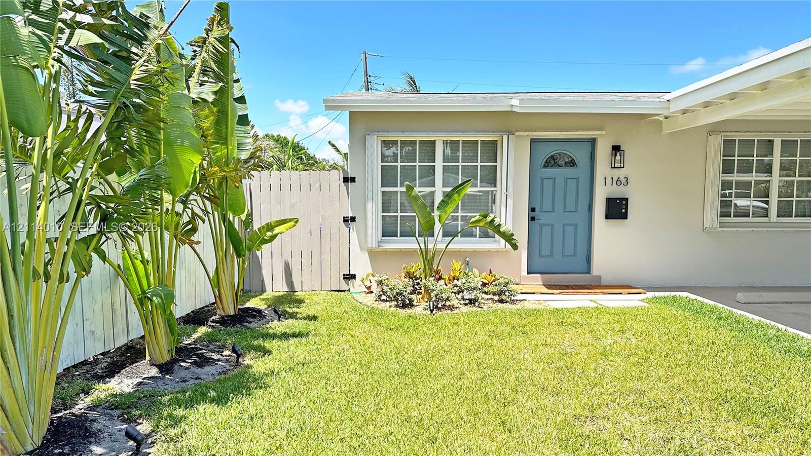 Exterior featuring light-toned stucco siding, a blue painted entry door, grid-pattern windows, an attached carport, and a fenced perimeter