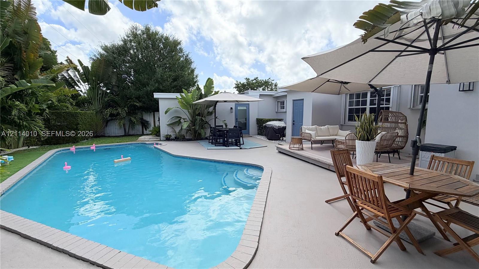 In-ground swimming pool with integrated steps, expansive paved patio, and mature landscaping