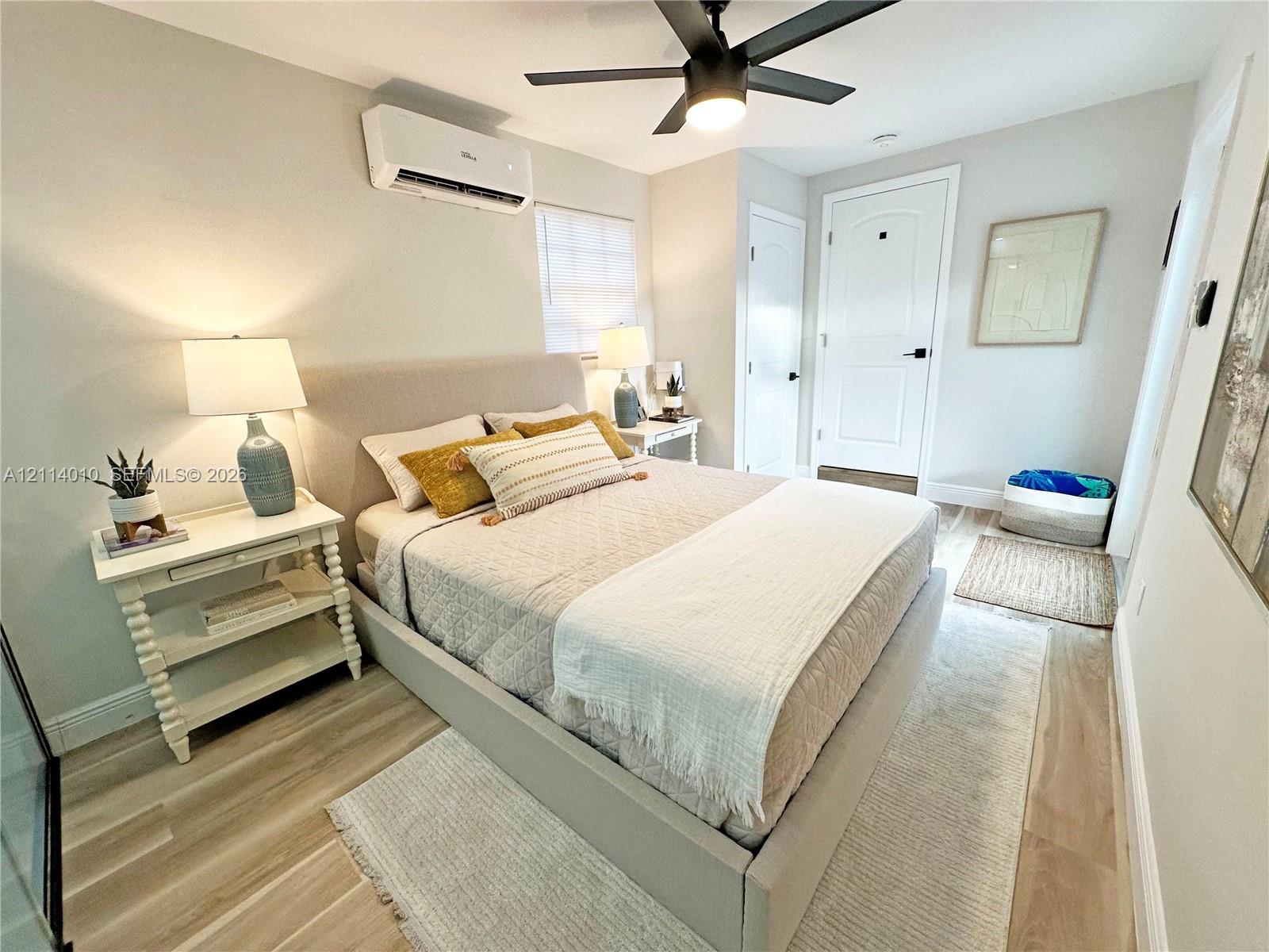 Room featuring wood-finish flooring, a wall-mounted ductless air conditioning unit, a matte black ceiling fan with an integrated light, and a white interior door with a matte black lever handle