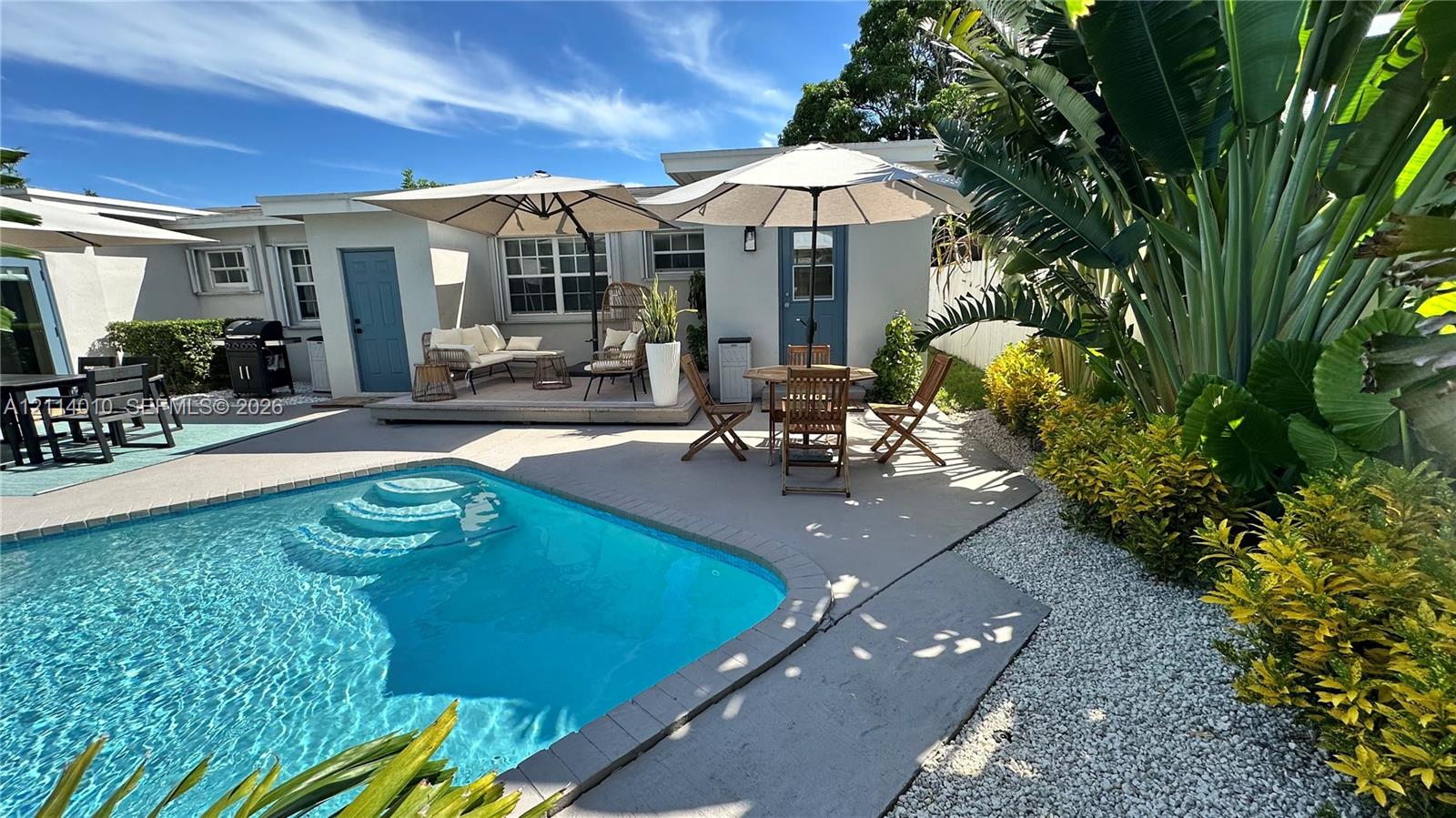 Outdoor space featuring an in-ground swimming pool, concrete patio, gravel landscaping, and mature tropical greenery