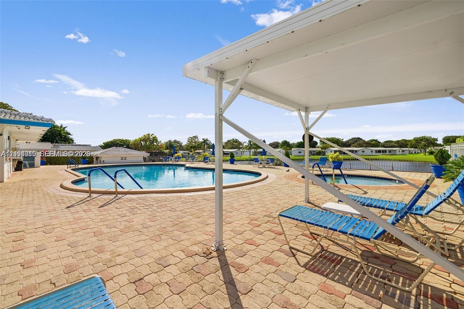 Outdoor swimming pool and spa area featuring a paved brick patio, covered pavilion, and water-side perimeter fencing
