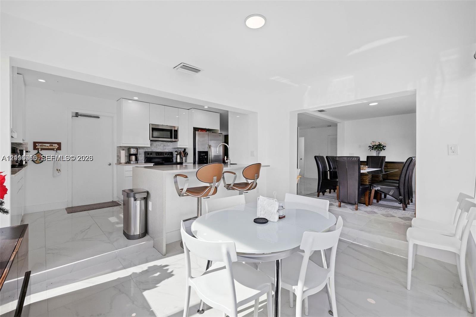 Kitchen featuring white flat-panel cabinetry, quartz countertops, a waterfall-edge breakfast bar, stainless steel appliances, and large-format porcelain tile flooring