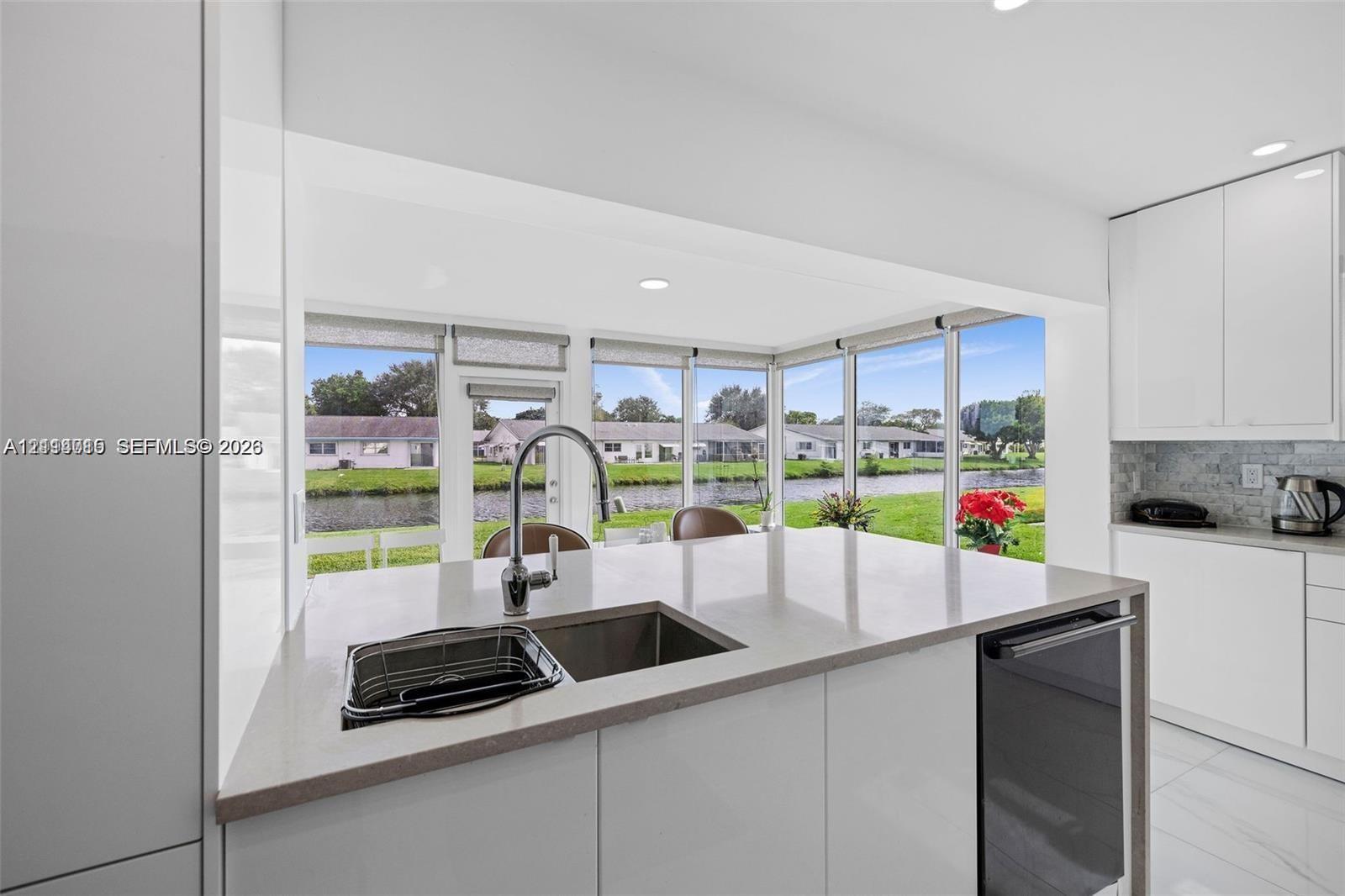 Kitchen featuring an island with a quartz countertop, undermount sink, high-arc faucet, white cabinetry, and floor-to-ceiling windows