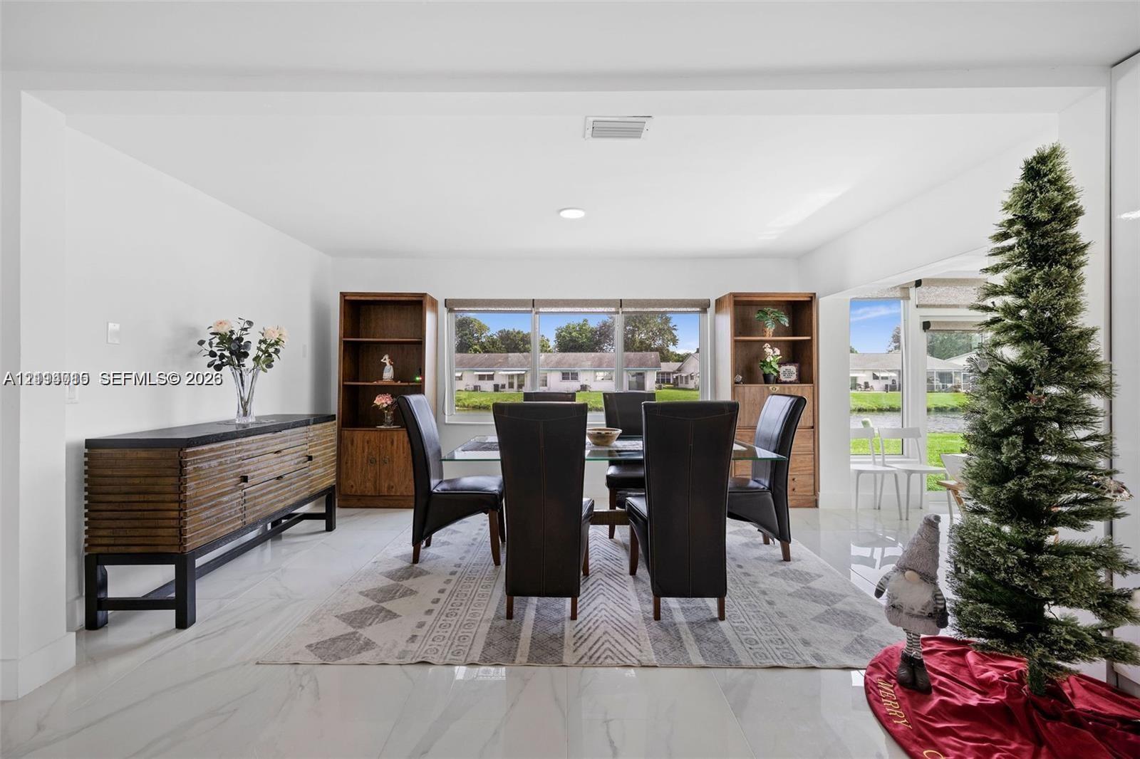 Open-concept area featuring polished light-toned tile flooring, dual built-in floor-to-ceiling wooden shelving units, and large windows with water exposure