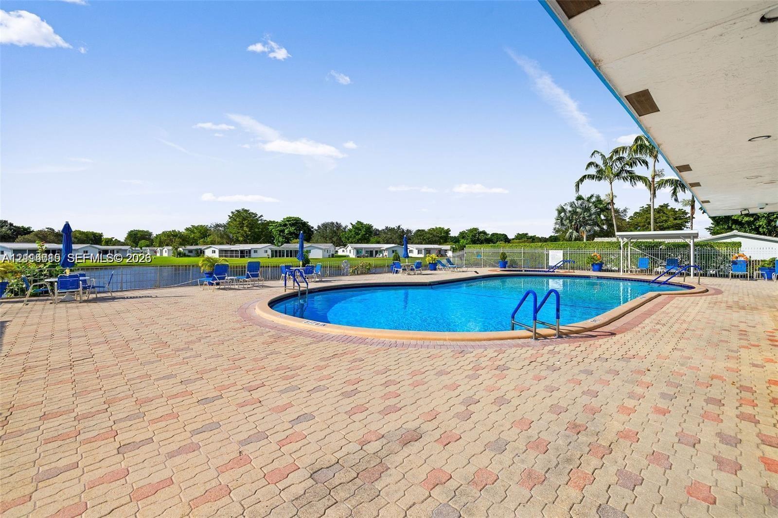 Inground swimming pool with metal ladder access, bordered by a multi-tone paver patio and decorative tile edging