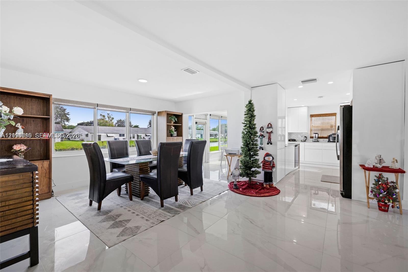 Open-concept space featuring polished stone-finish flooring, recessed lighting, expansive windows, built-in shelving units, and a kitchen equipped with white cabinetry